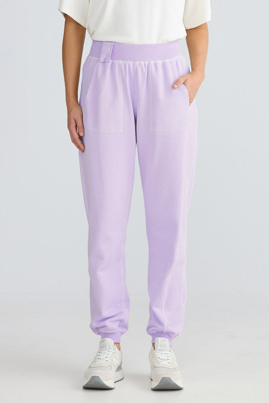 Woman wearing a white top and light purple pants on a plain background