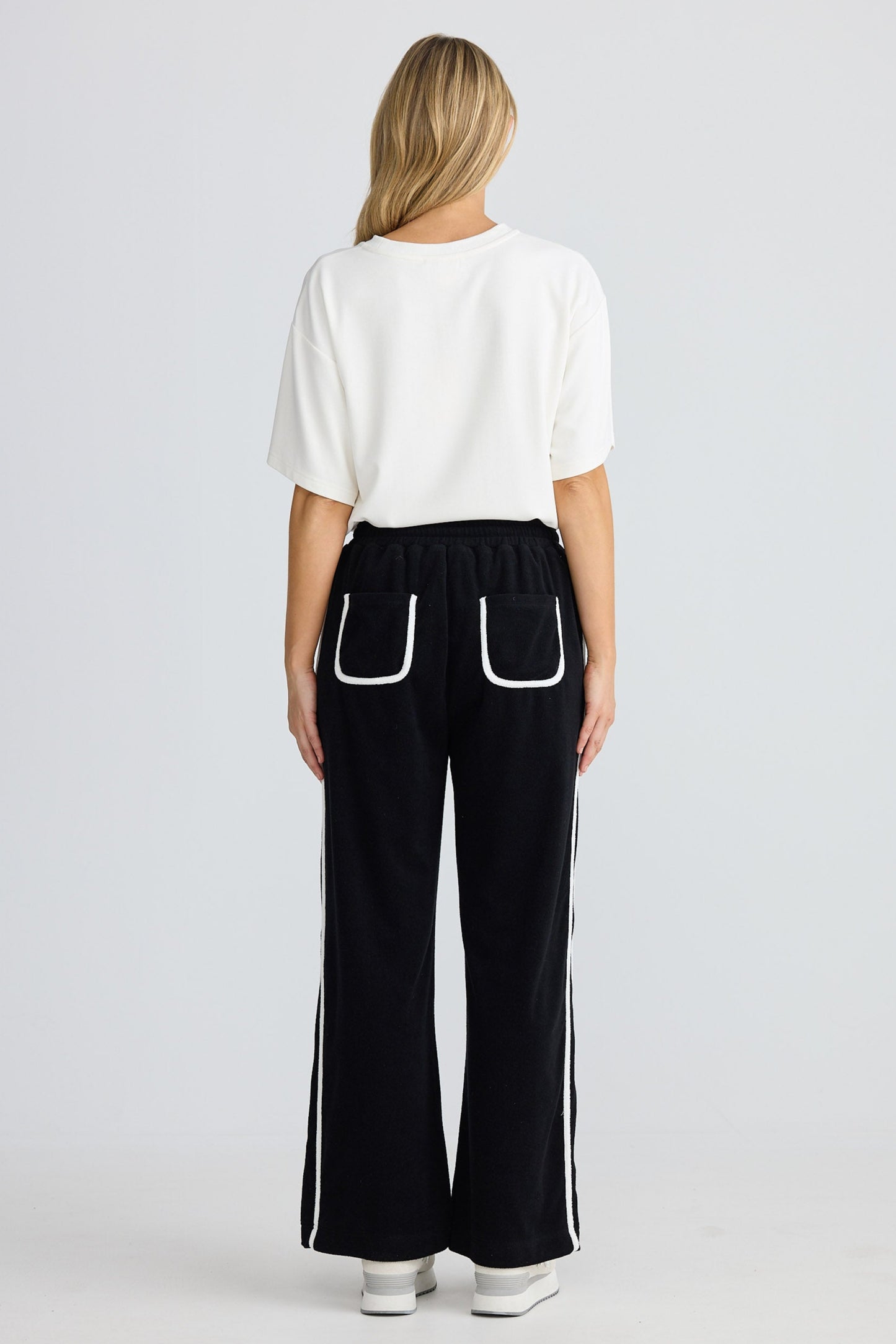 Person wearing a white top and black pants with white trim on a white background