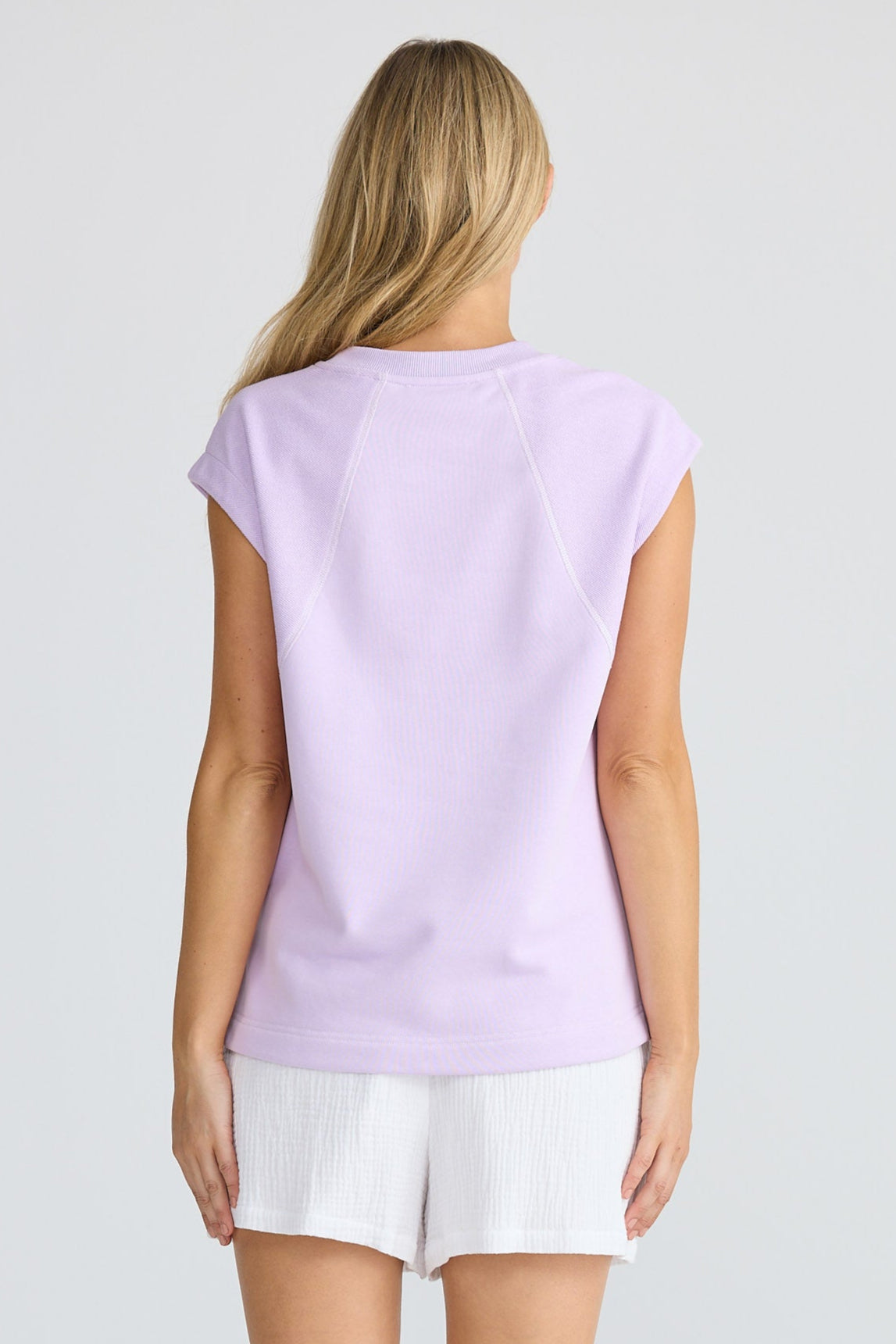 Woman wearing a light purple t-shirt and white shorts on a plain background