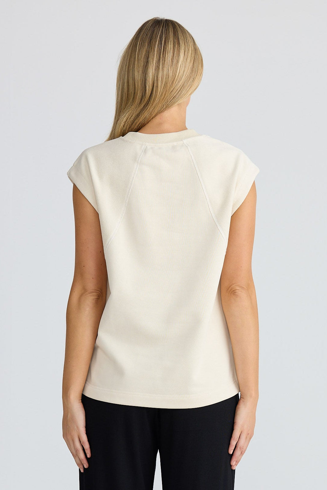 Woman wearing a white sleeveless top and black pants on a white background