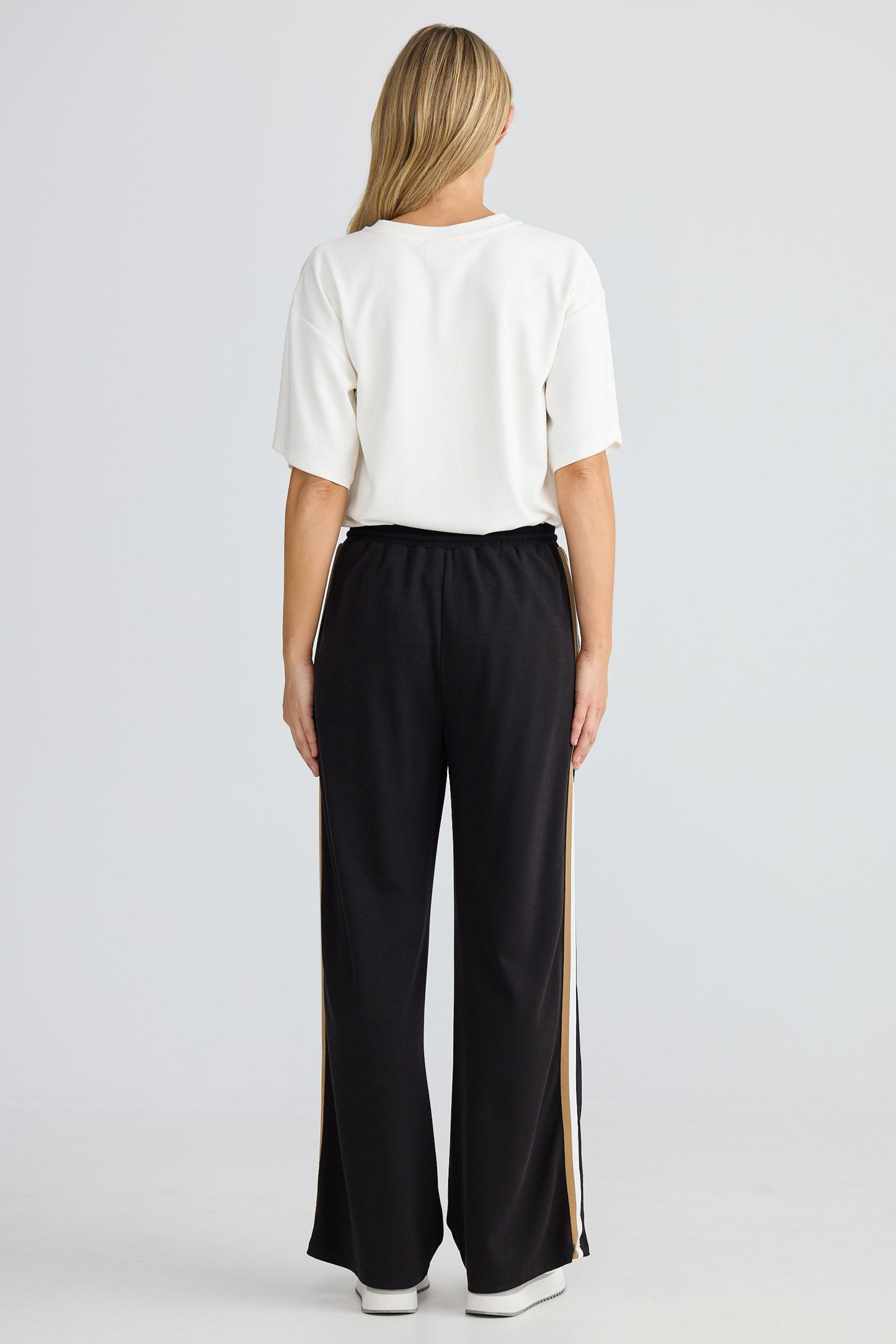 Person wearing a white top and black pants with a stripe on a white background