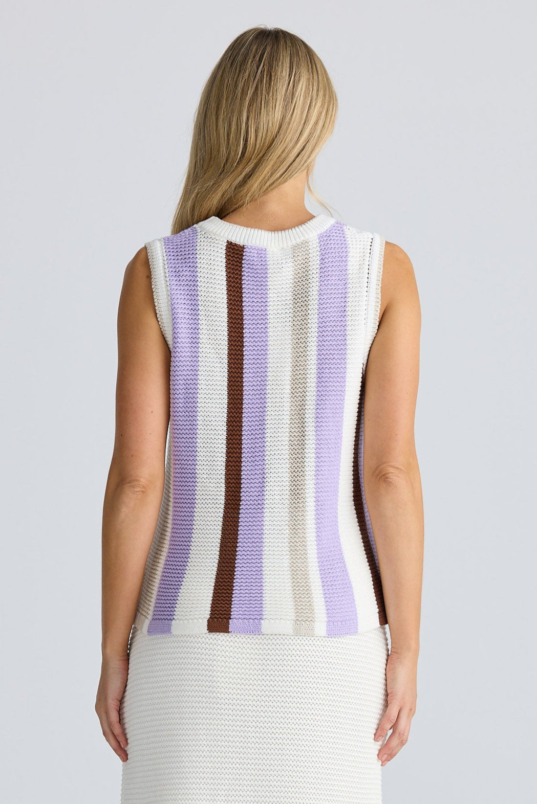 Woman wearing a sleeveless striped top and white pants on a plain background