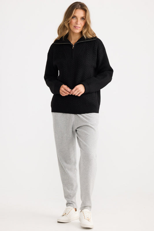 Woman wearing a black fleece jacket and gray pants on a white background