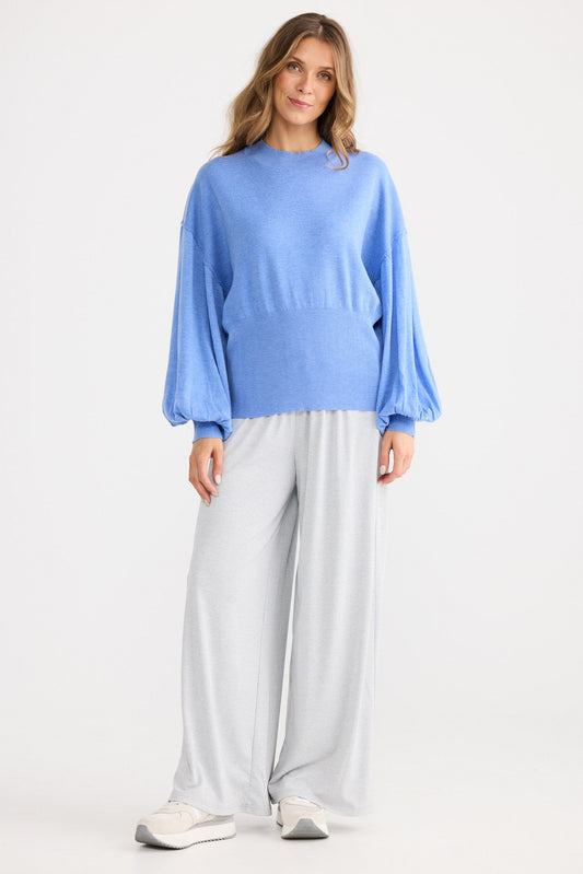 Woman wearing a blue sweater and light gray pants on a white background