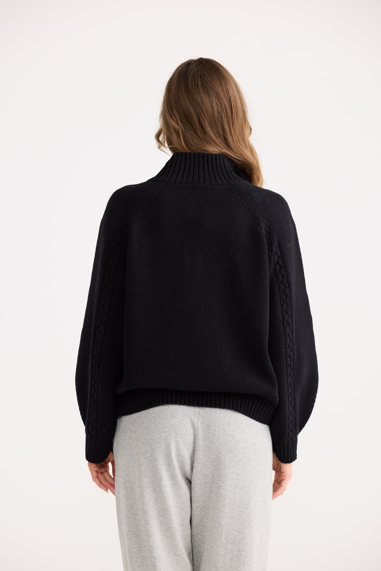 Person wearing a black sweater and light gray pants on a white background