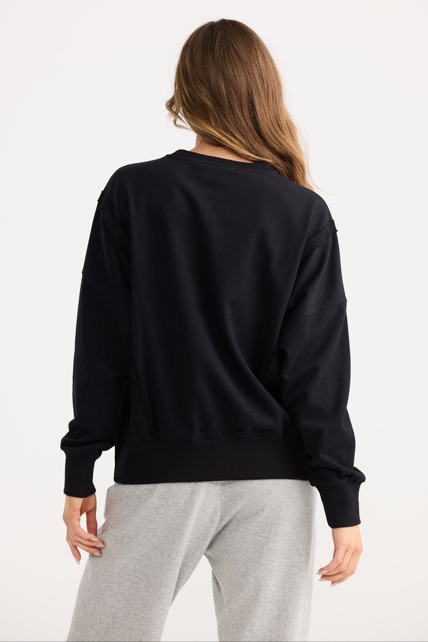 Person wearing a black sweater and gray pants on a white background