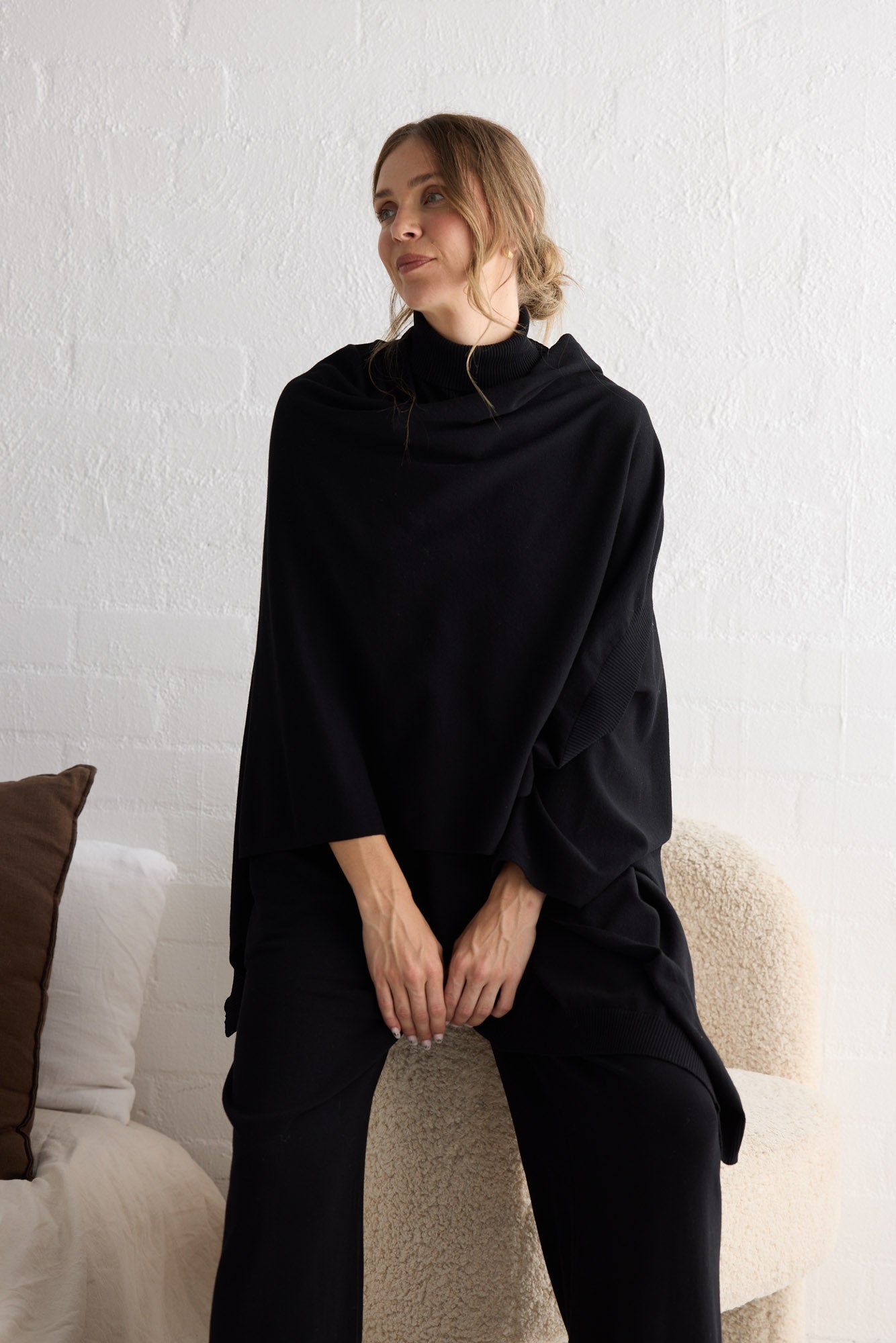 Campaign image of model wearing Awaken Knit Cape in black.