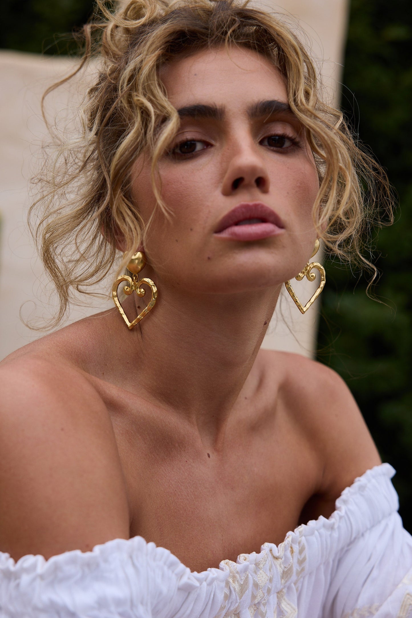 Woman wearing gold heart-shaped earrings with a blurred background
