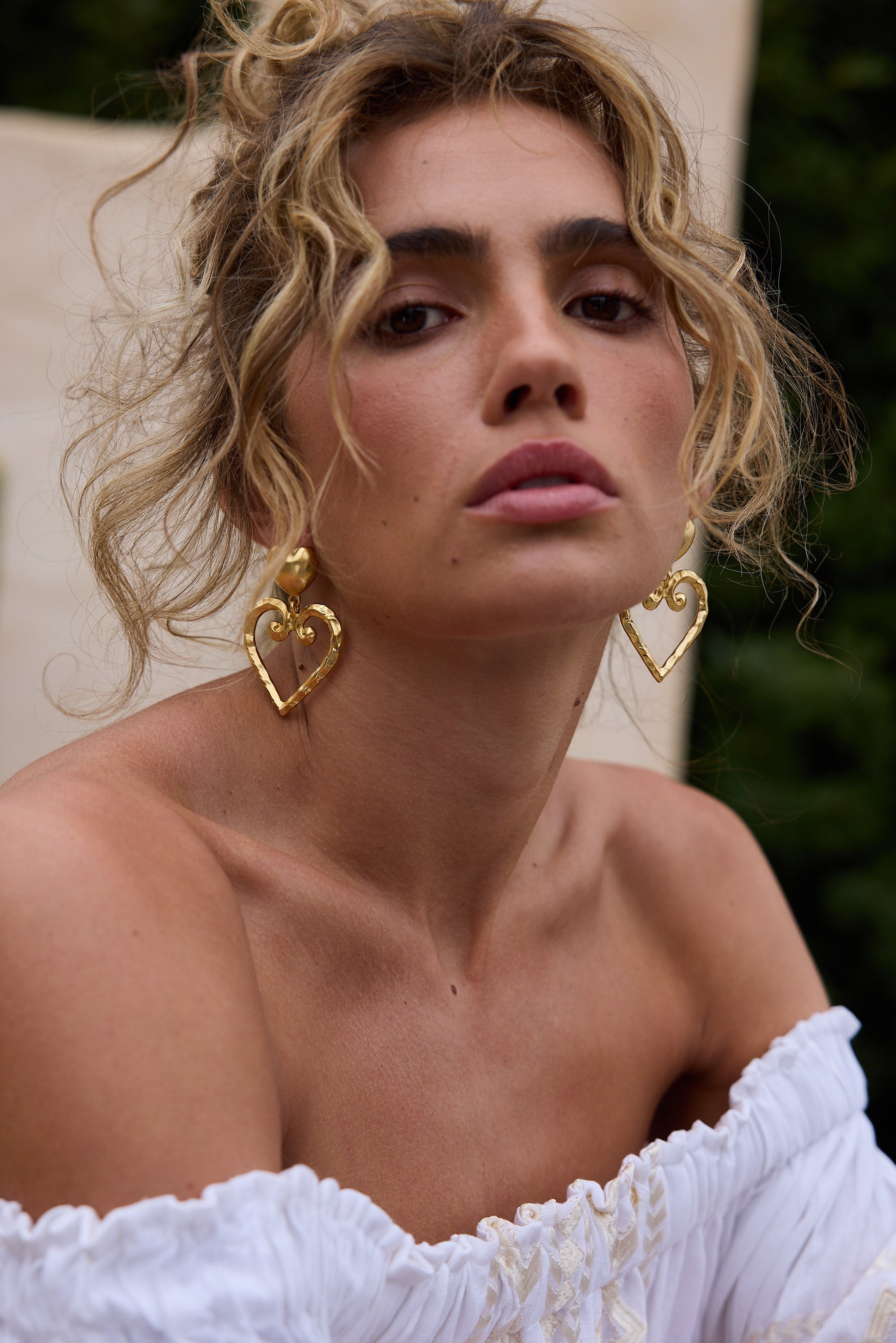 Woman wearing gold heart-shaped earrings with a blurred background