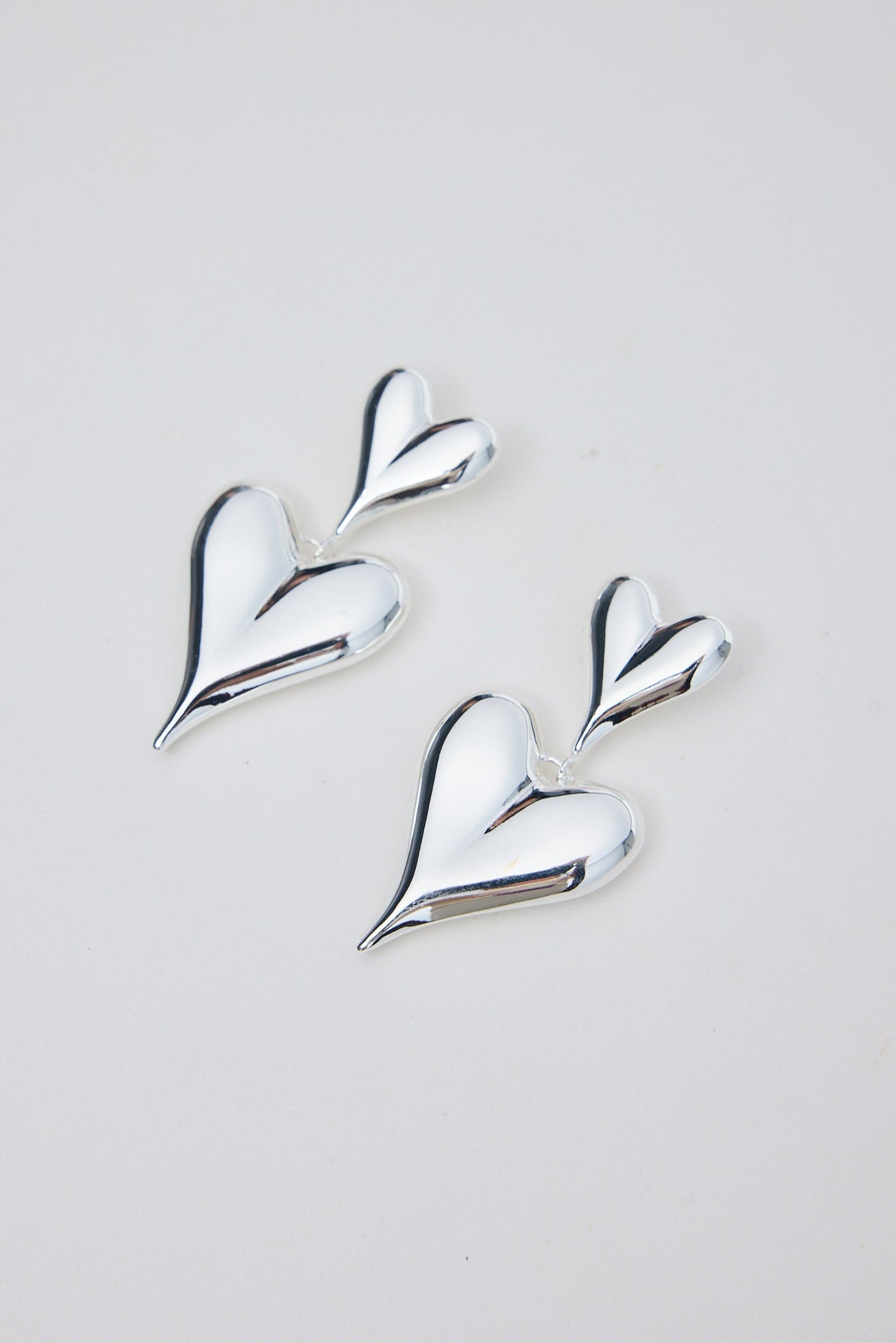 Silver heart-shaped earrings on a light gray background