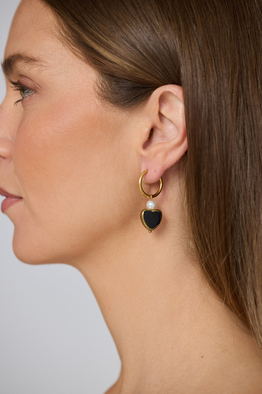 Model wearing Mimi Earrings in black with bold heart charm detail, model close-up view on neutral background