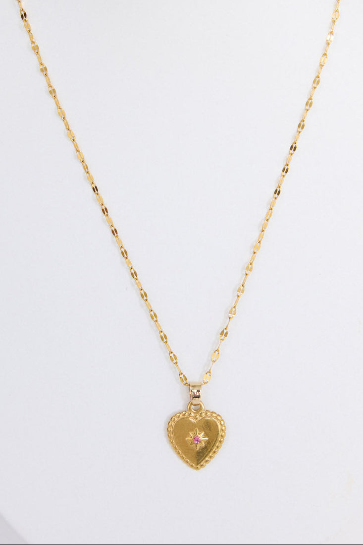 Aura Necklace in gold with heart pendant and stone detail, neckline styled view on neutral background