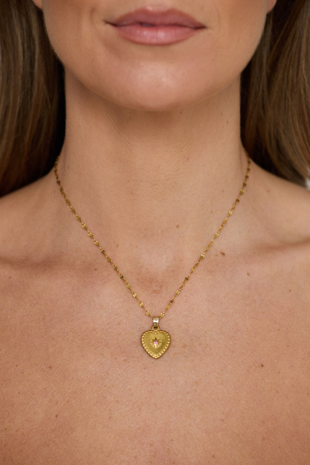 Aura Necklace in gold with heart pendant and stone detail, pendant close-up view on neutral background