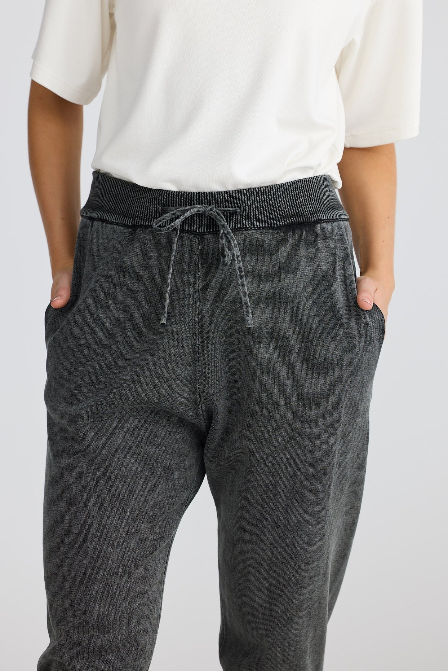 Person wearing dark gray jogger pants with a white top on a light gray background