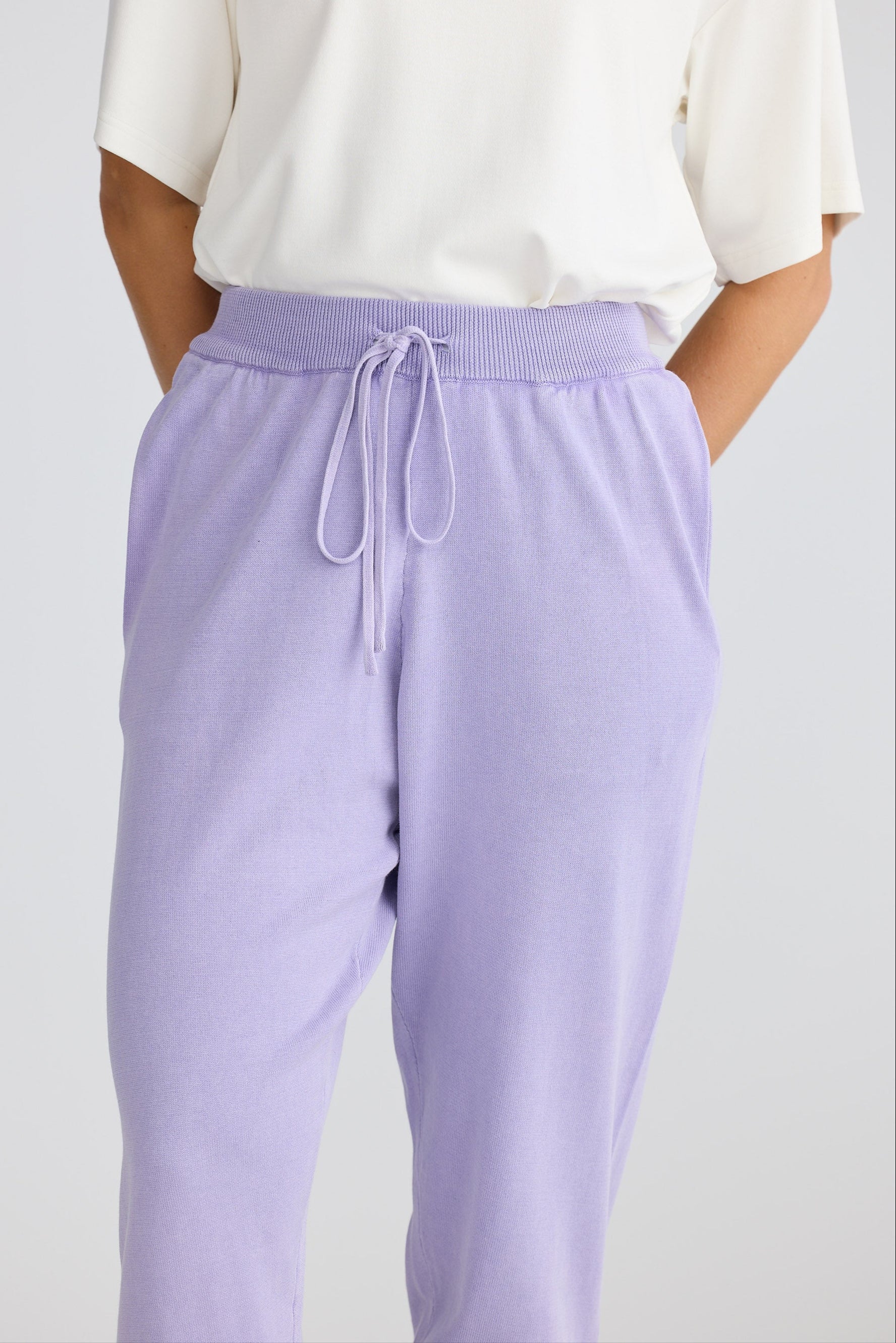 Person wearing a white top and lavender pants with a drawstring on a light gray background