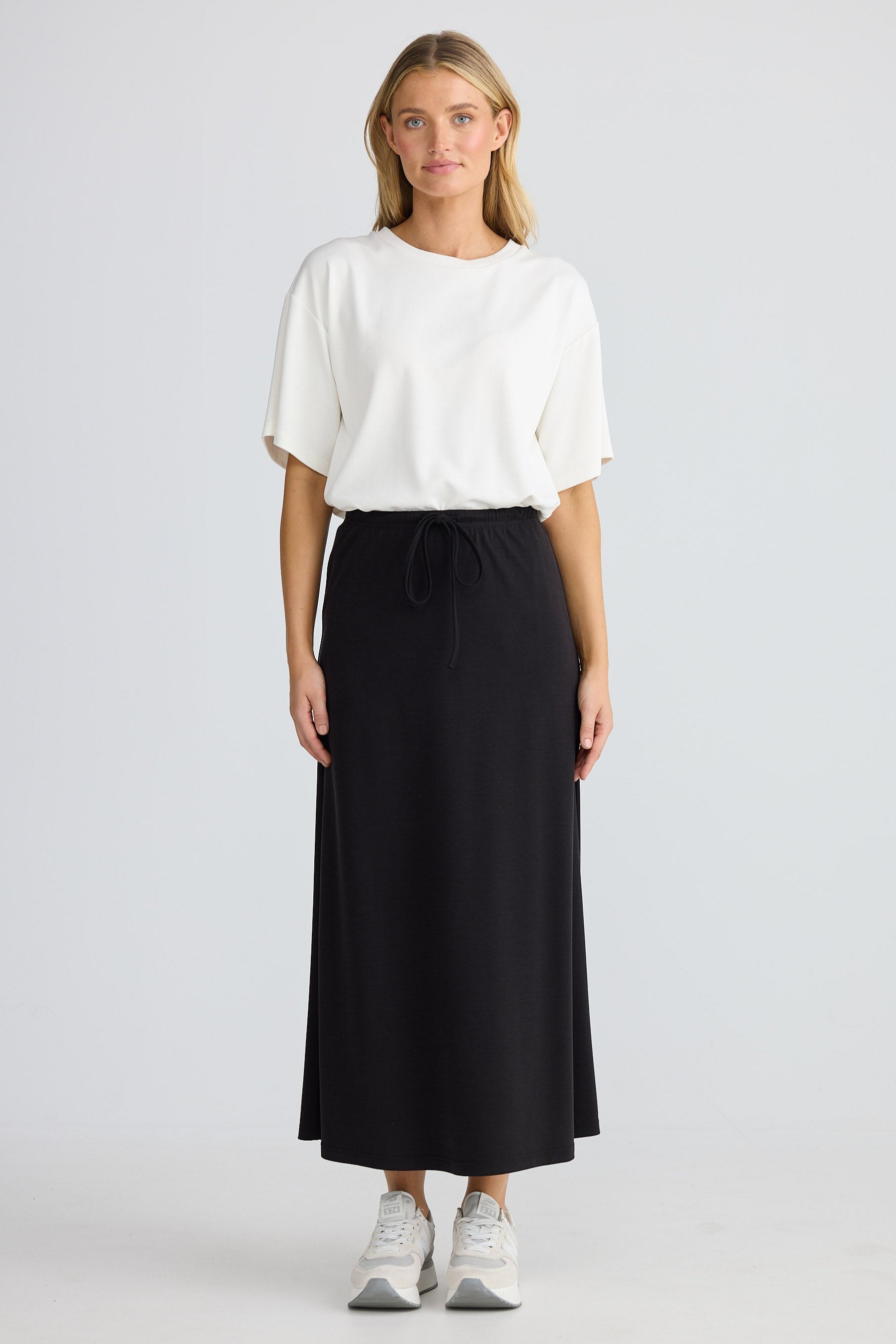 Woman wearing a white t-shirt and black skirt on a plain background