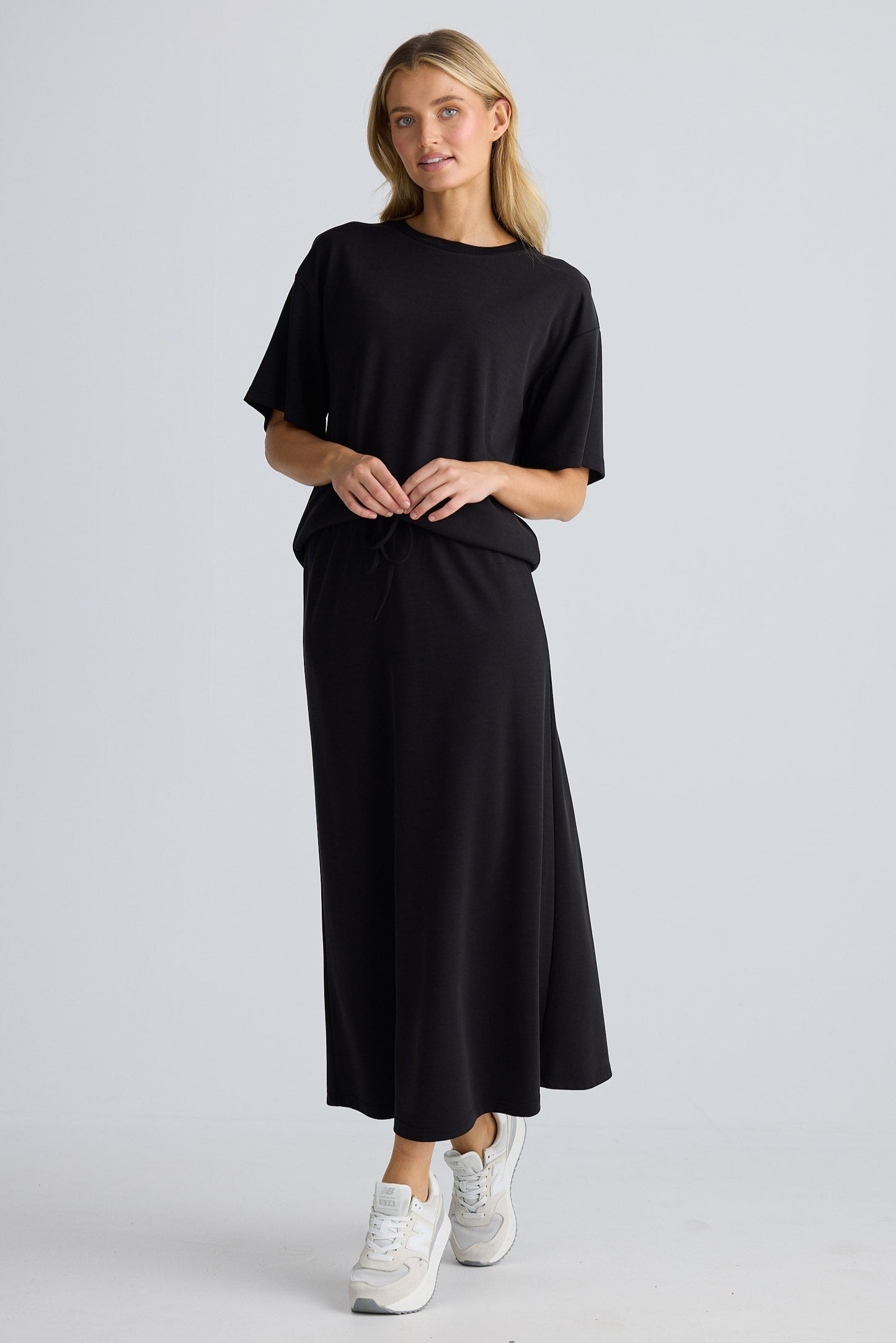 Woman wearing a black outfit with white sneakers on a light gray background