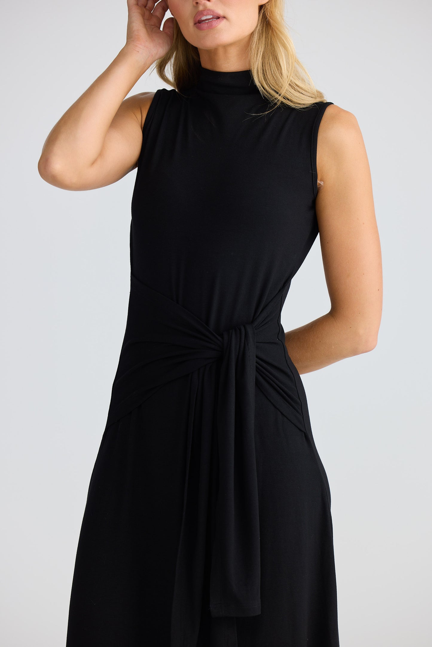 Woman wearing a black sleeveless dress against a plain background
