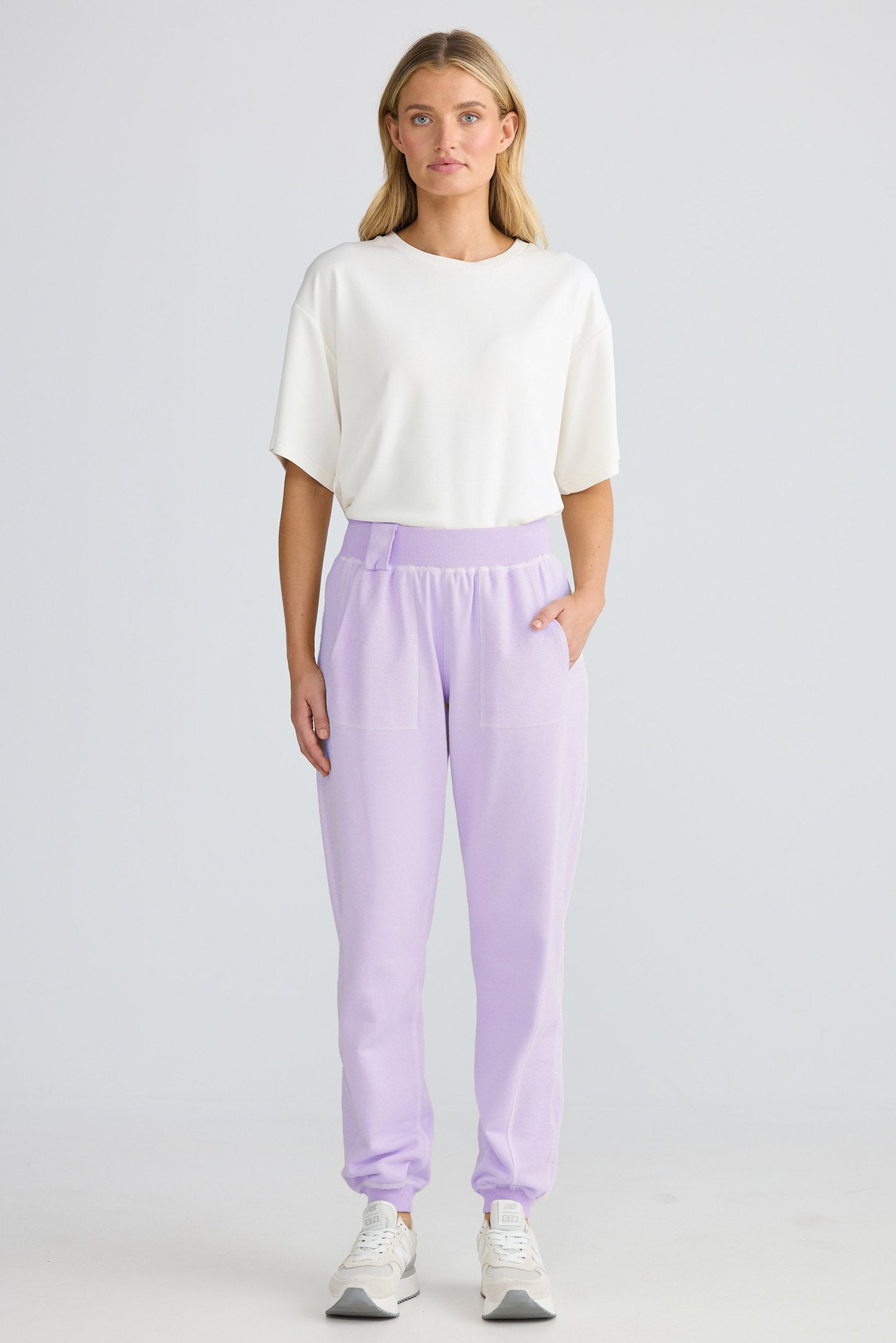 Woman wearing a white top and lavender pants on a plain background