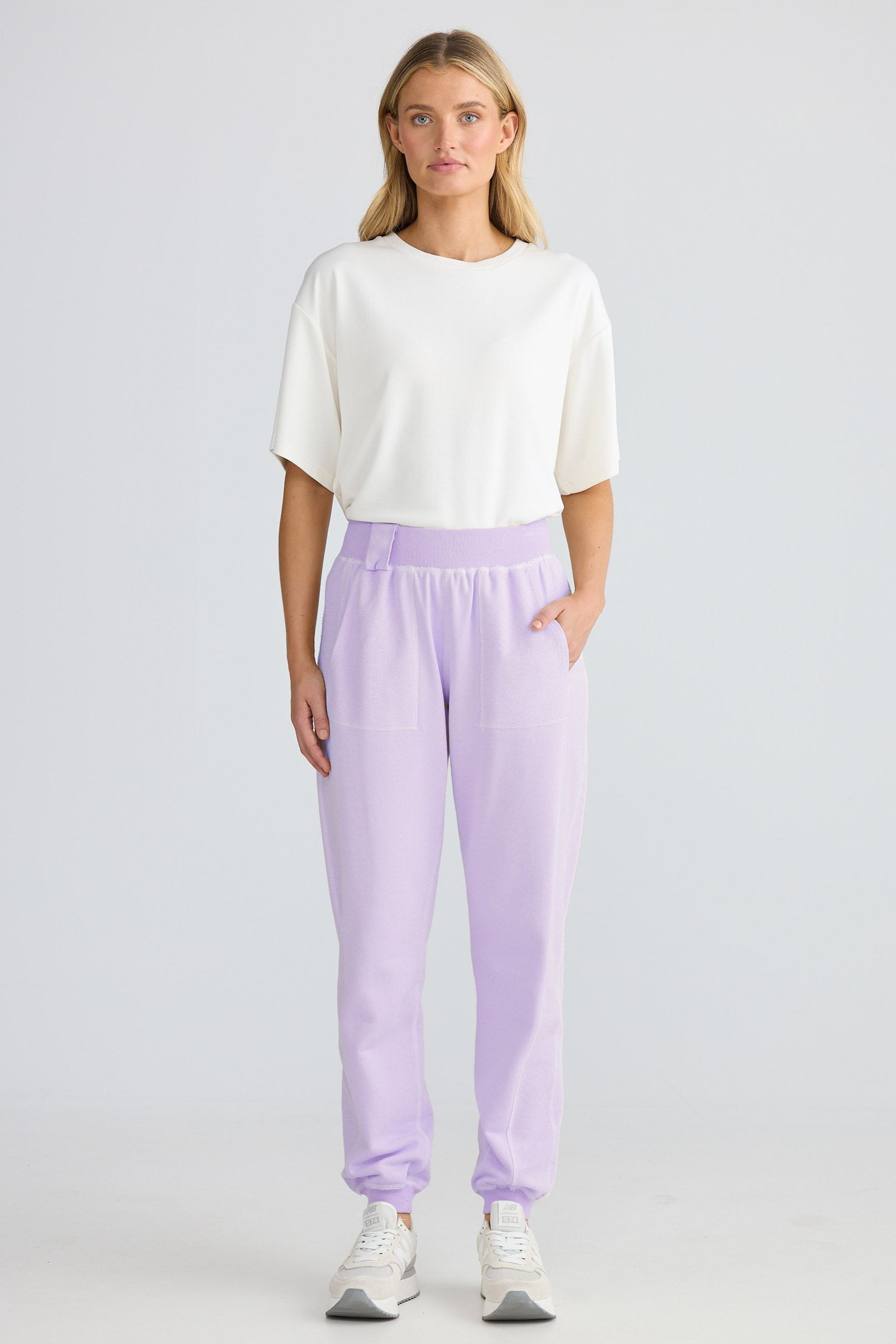 Woman wearing a white top and lavender pants on a plain background