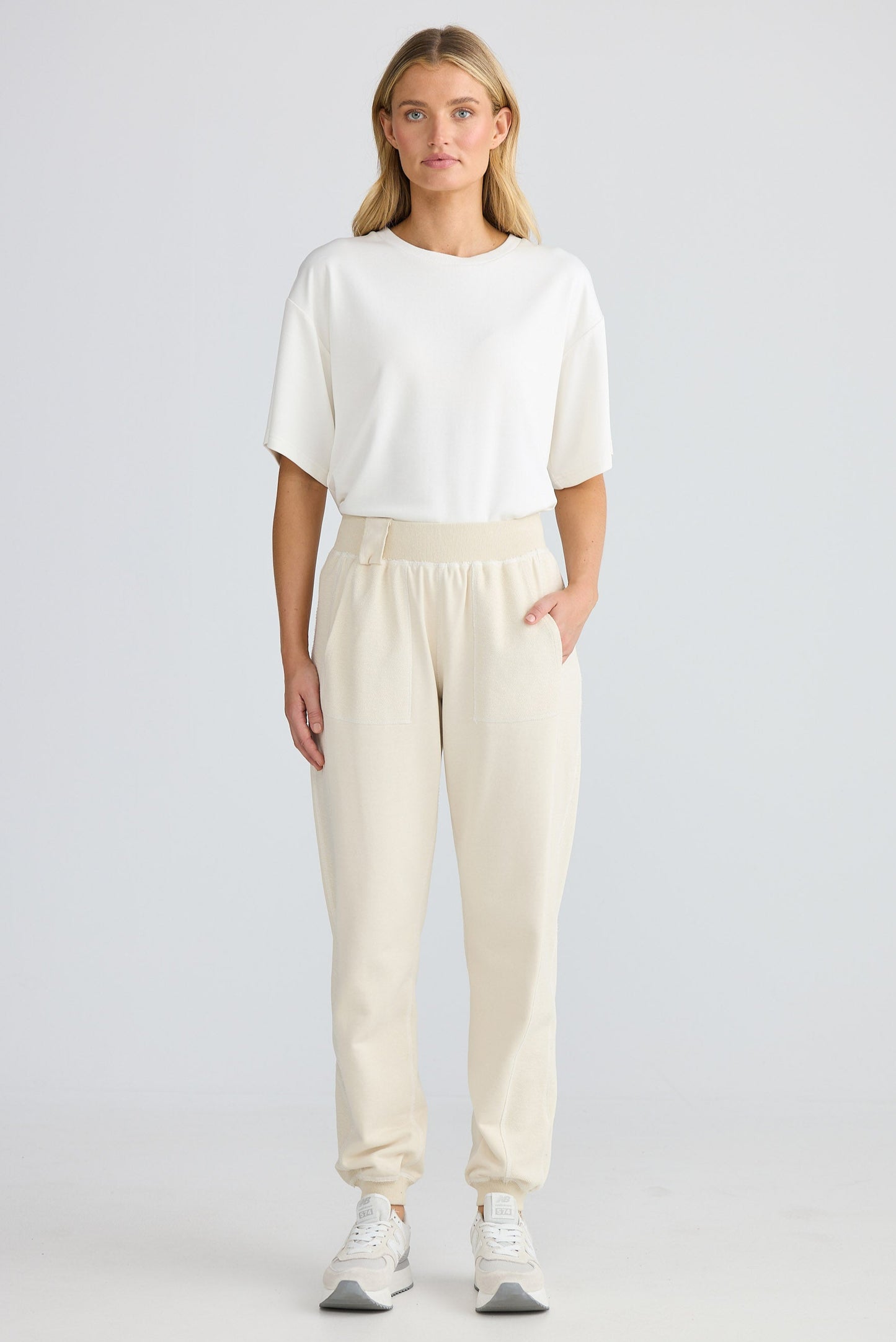 Woman wearing a white top and beige pants on a plain background