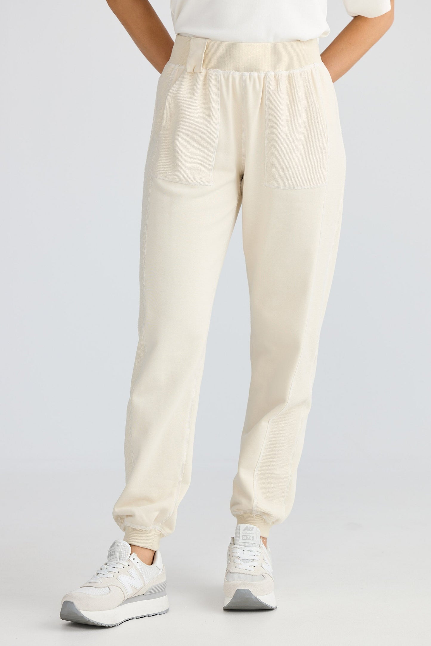 Person wearing beige jogger pants and white sneakers on a light gray background
