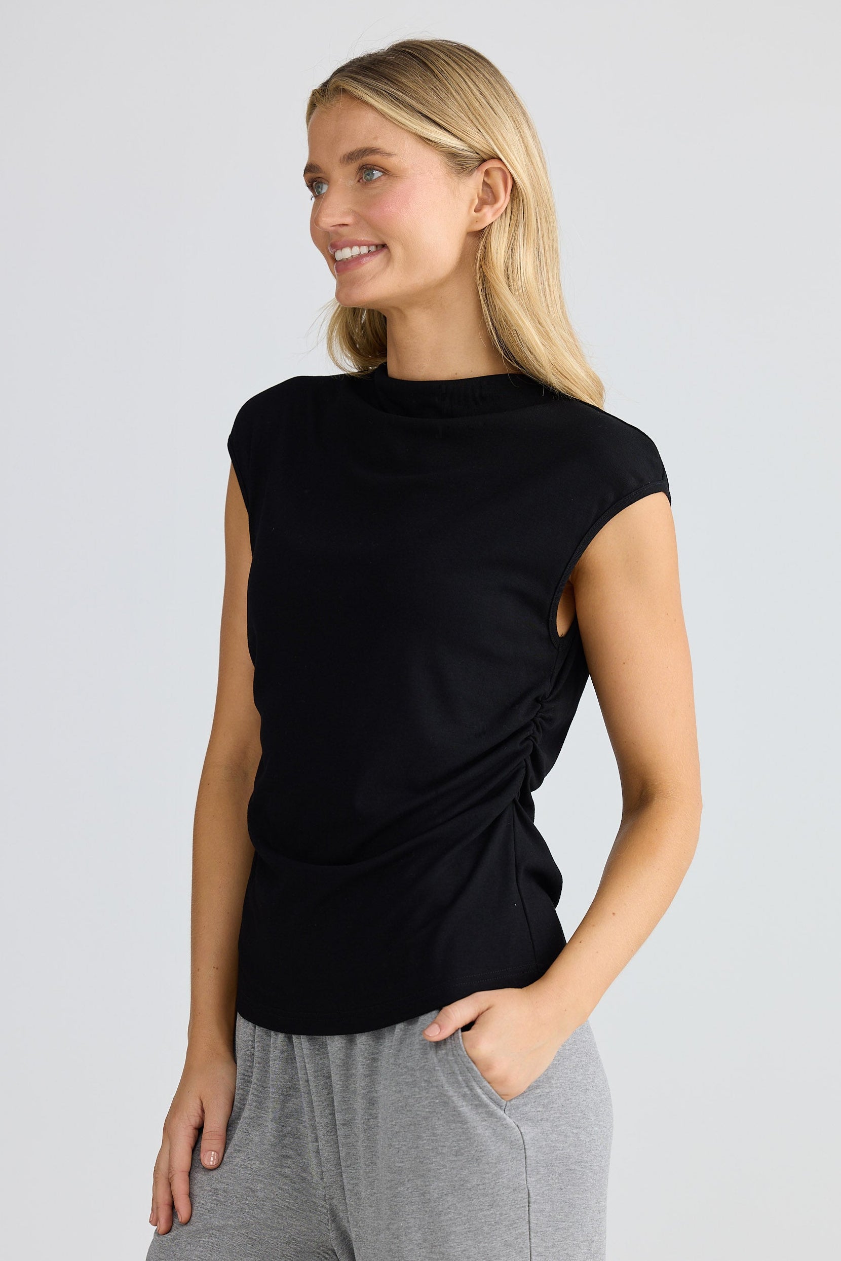 Woman wearing a black short sleeve top and gray pants against a white background