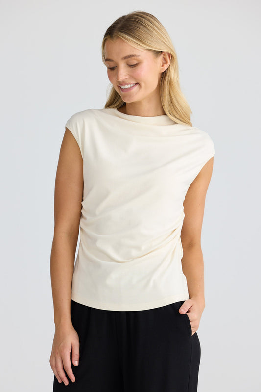 Woman wearing a cream short sleeve top and black pants on a white background