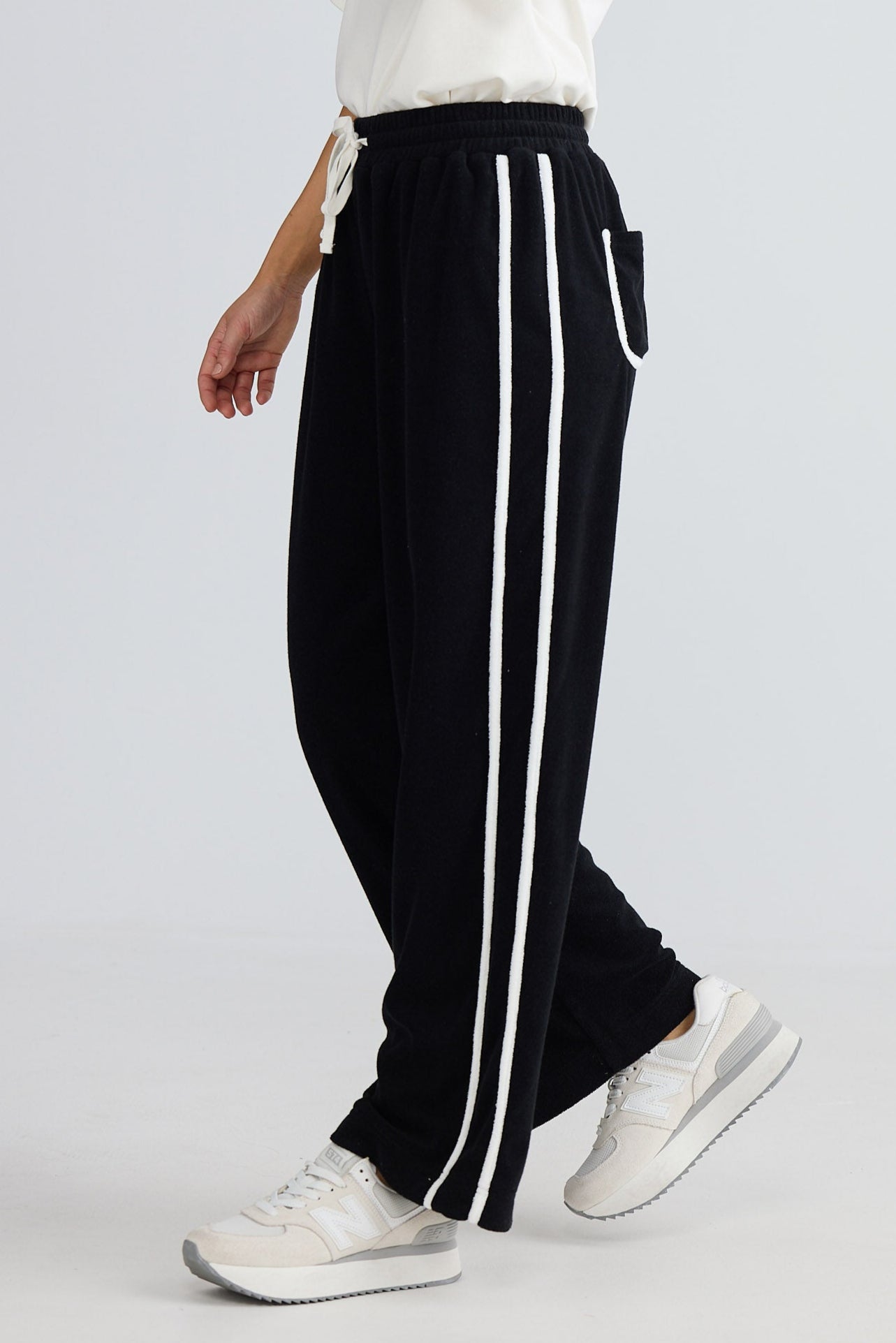 Woman wearing black pants with white stripes and a white top on a light gray background