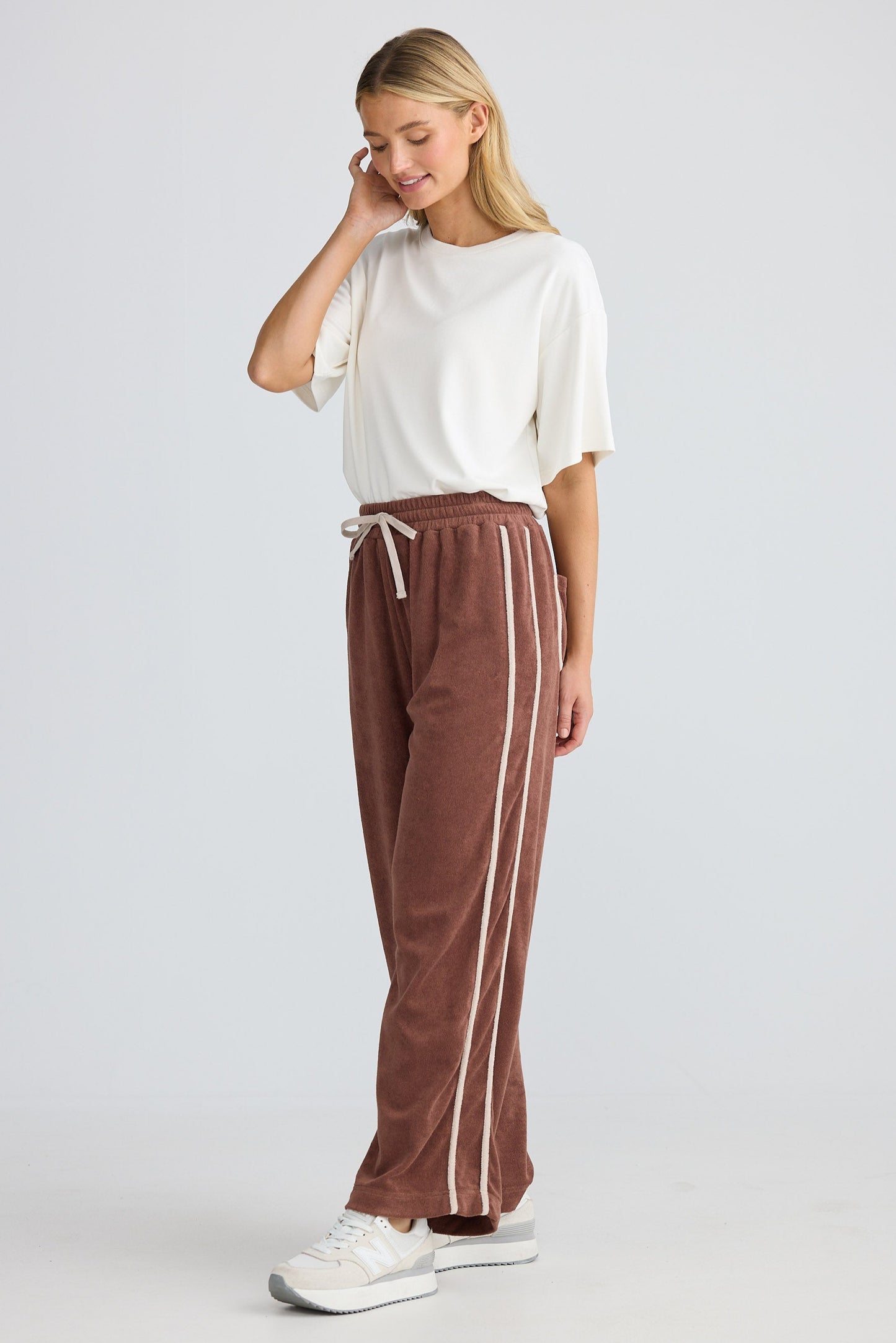 Woman wearing a white top and brown pants with a stripe on a plain background