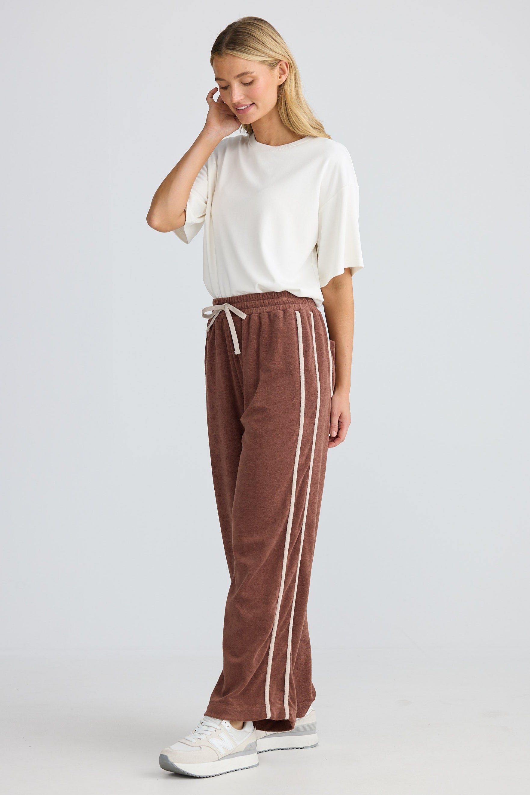 Woman wearing a white top and brown pants with a stripe on a plain background