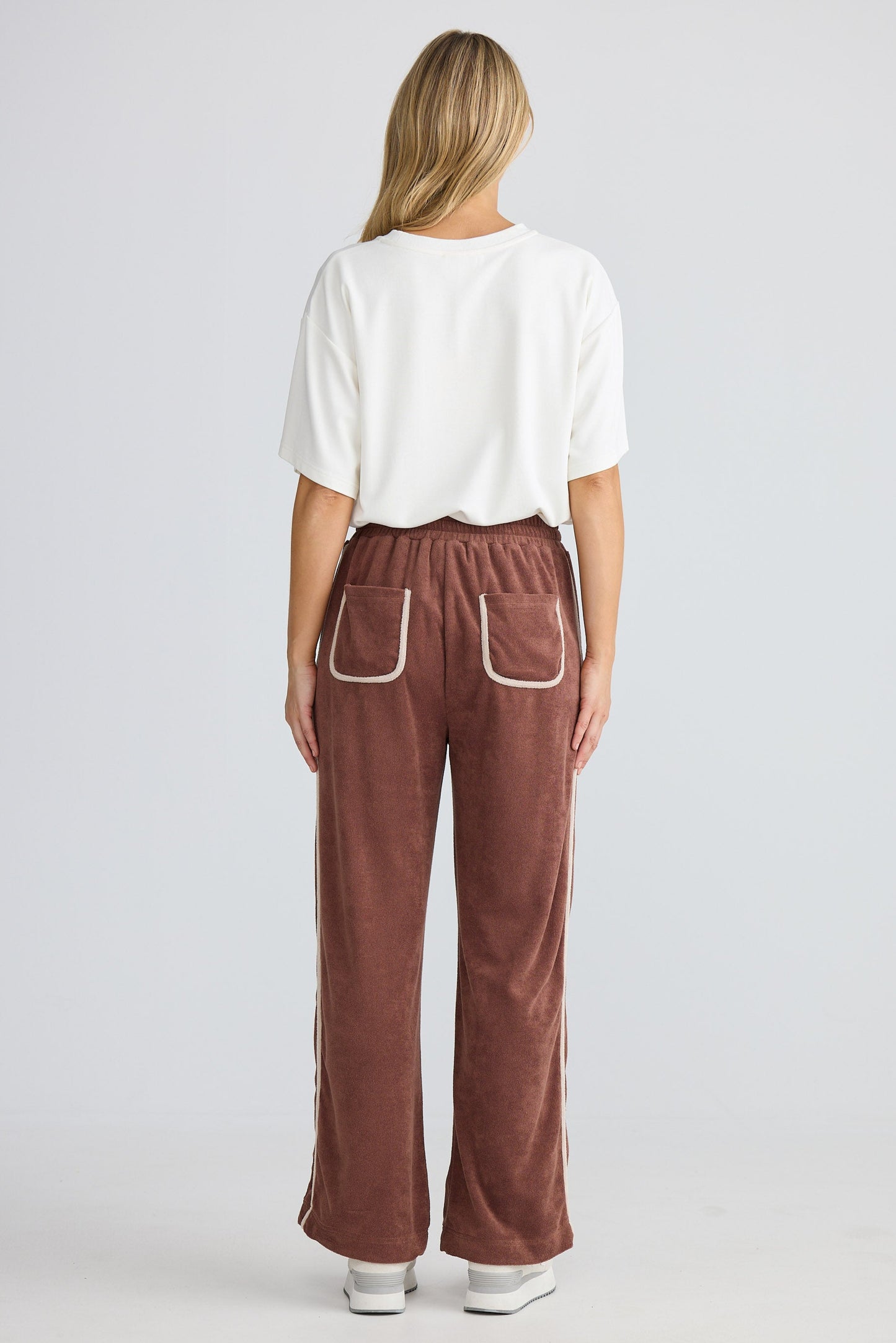 Person wearing brown pants with white trim on a plain background