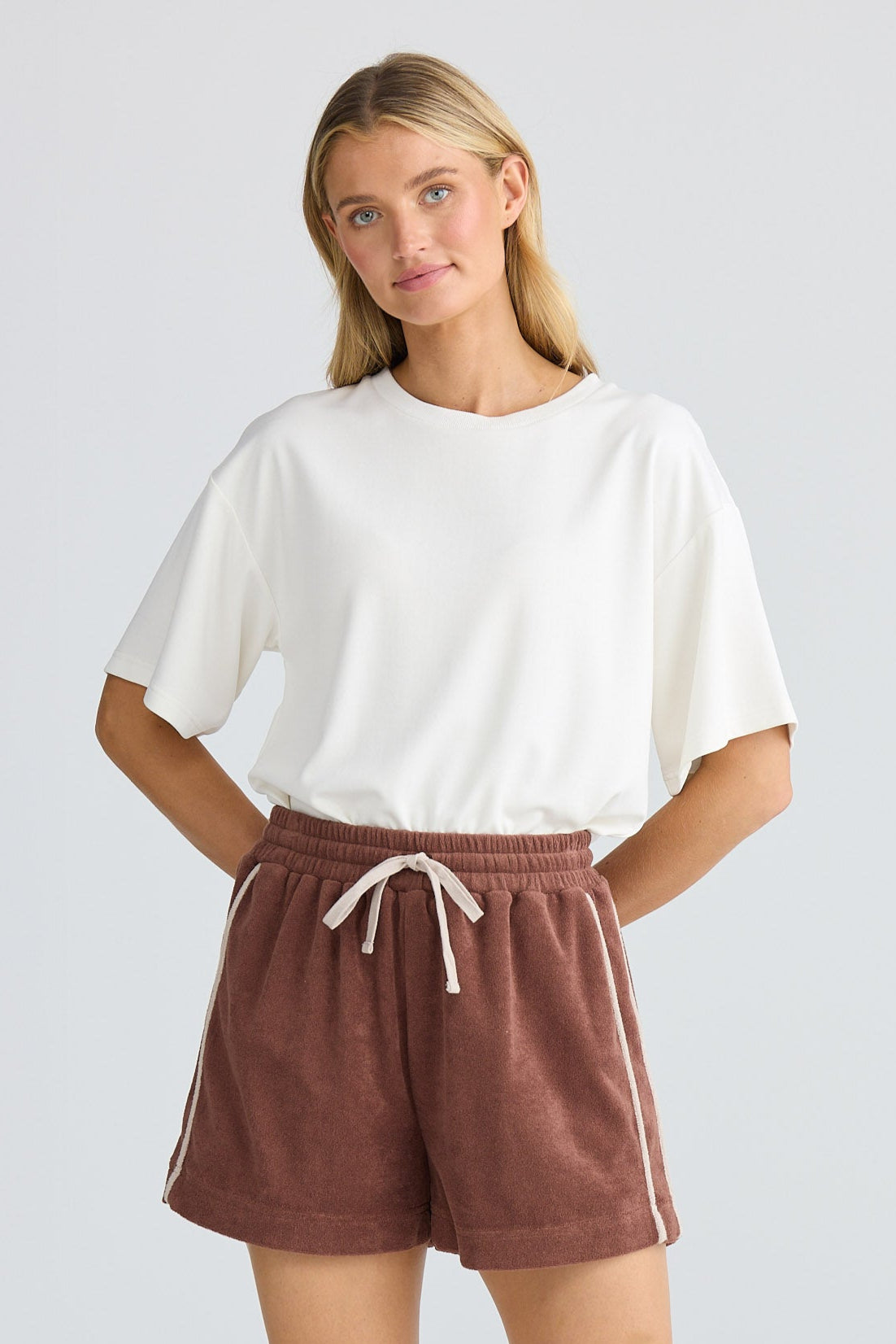 Woman wearing a white top and brown shorts on a plain background