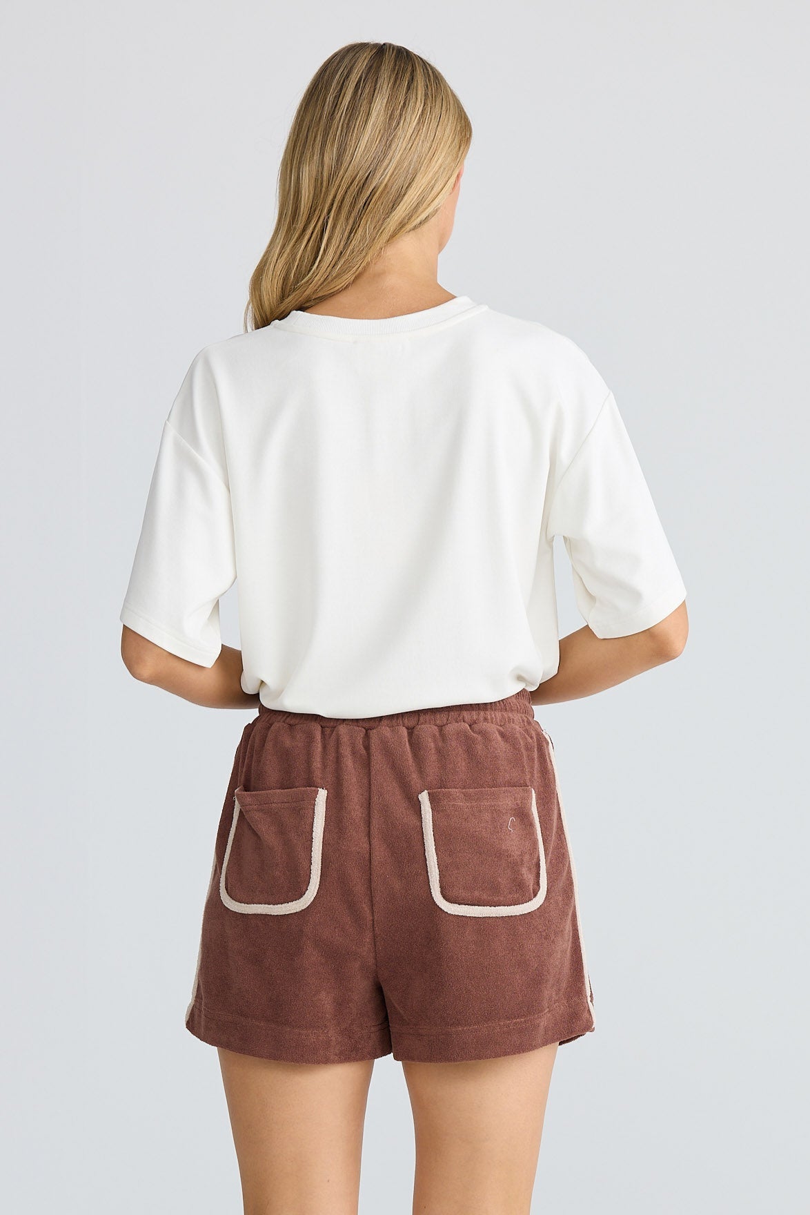 Person wearing brown shorts with white accents on a plain background