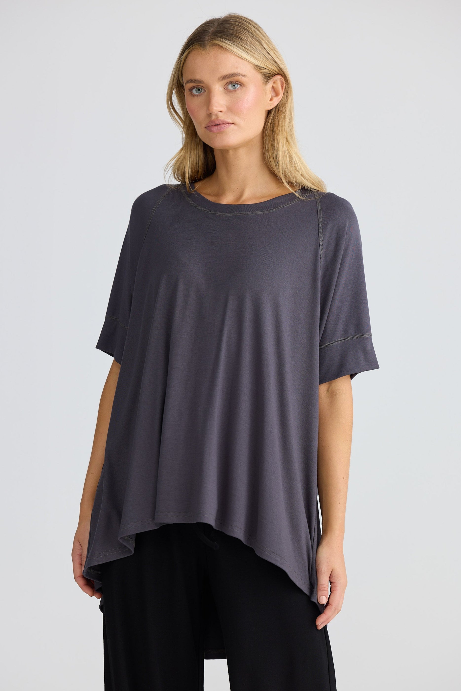 Woman wearing a dark grey oversized tee with black pants on a light gray background