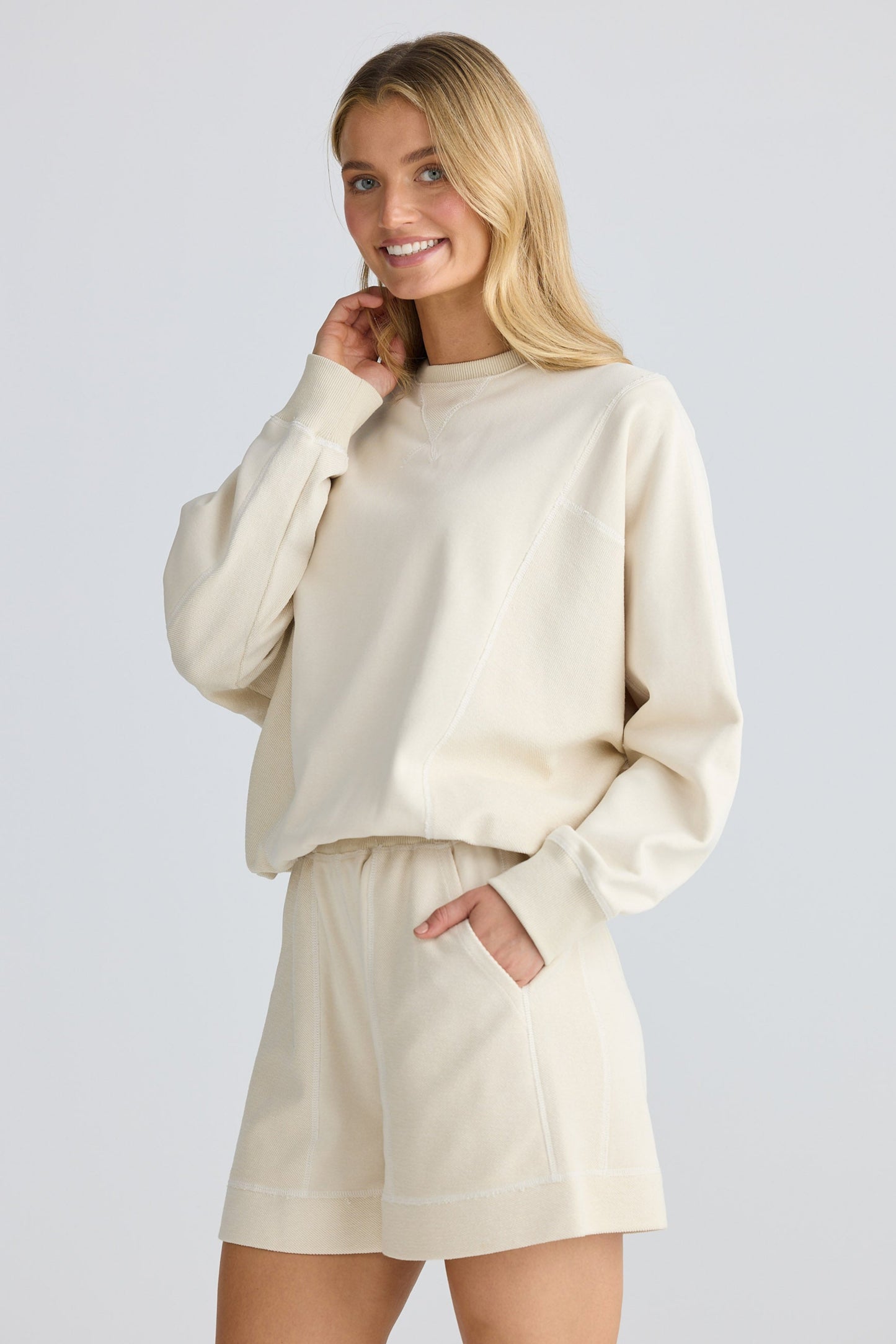 Woman wearing a beige sweater and shorts set on a light gray background