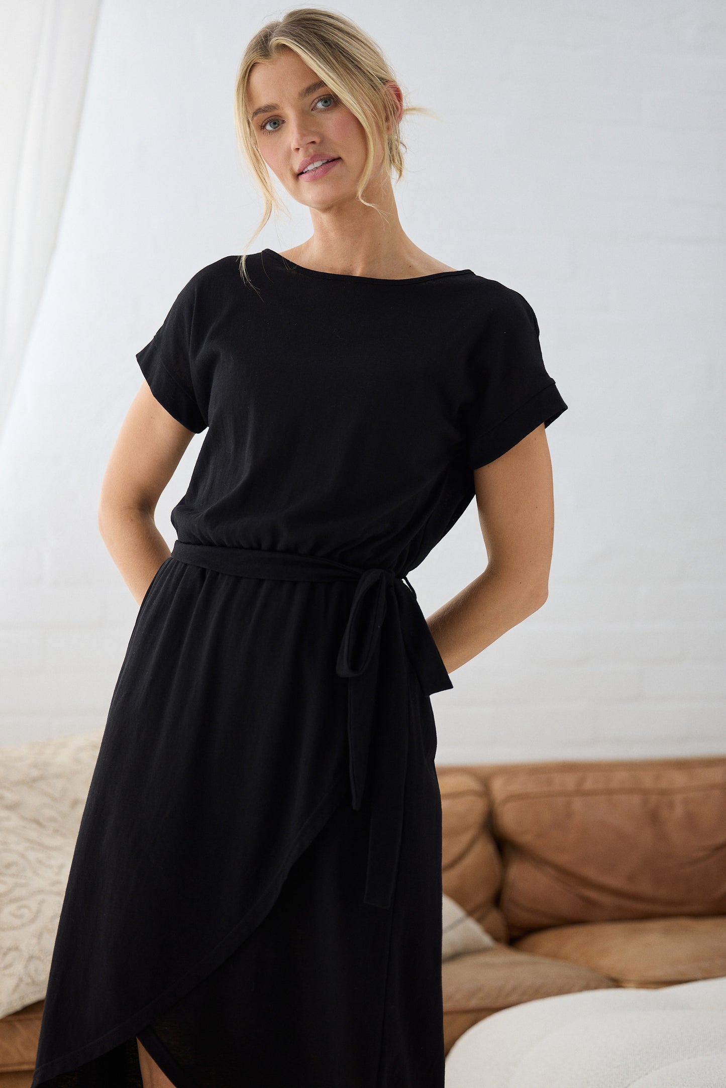 Woman wearing a black dress standing in a room with a couch and white wall.