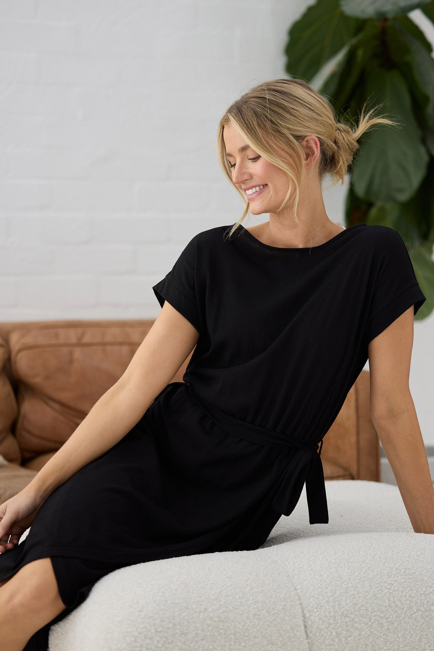 Woman wearing a black dress sitting on a couch with a plant in the background