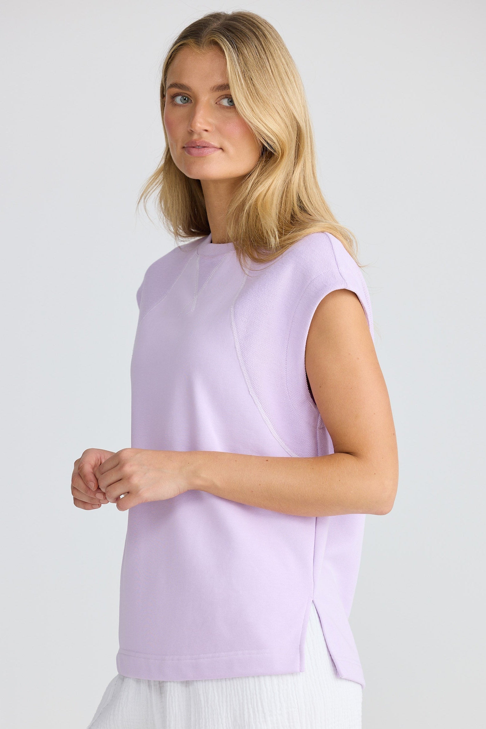 Woman wearing a light purple sleeveless top and white skirt on a plain background