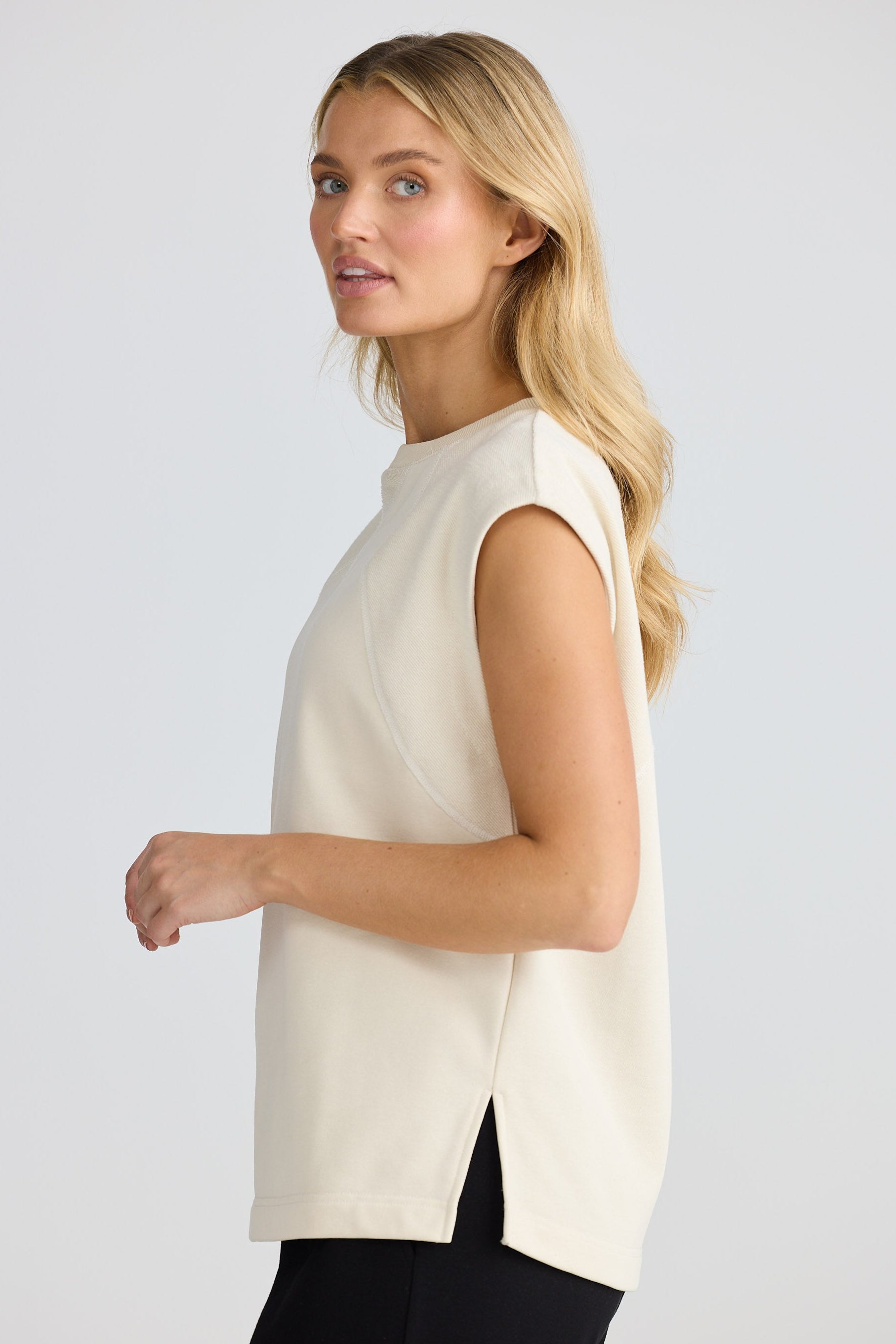 Woman wearing a white sleeveless top against a plain background