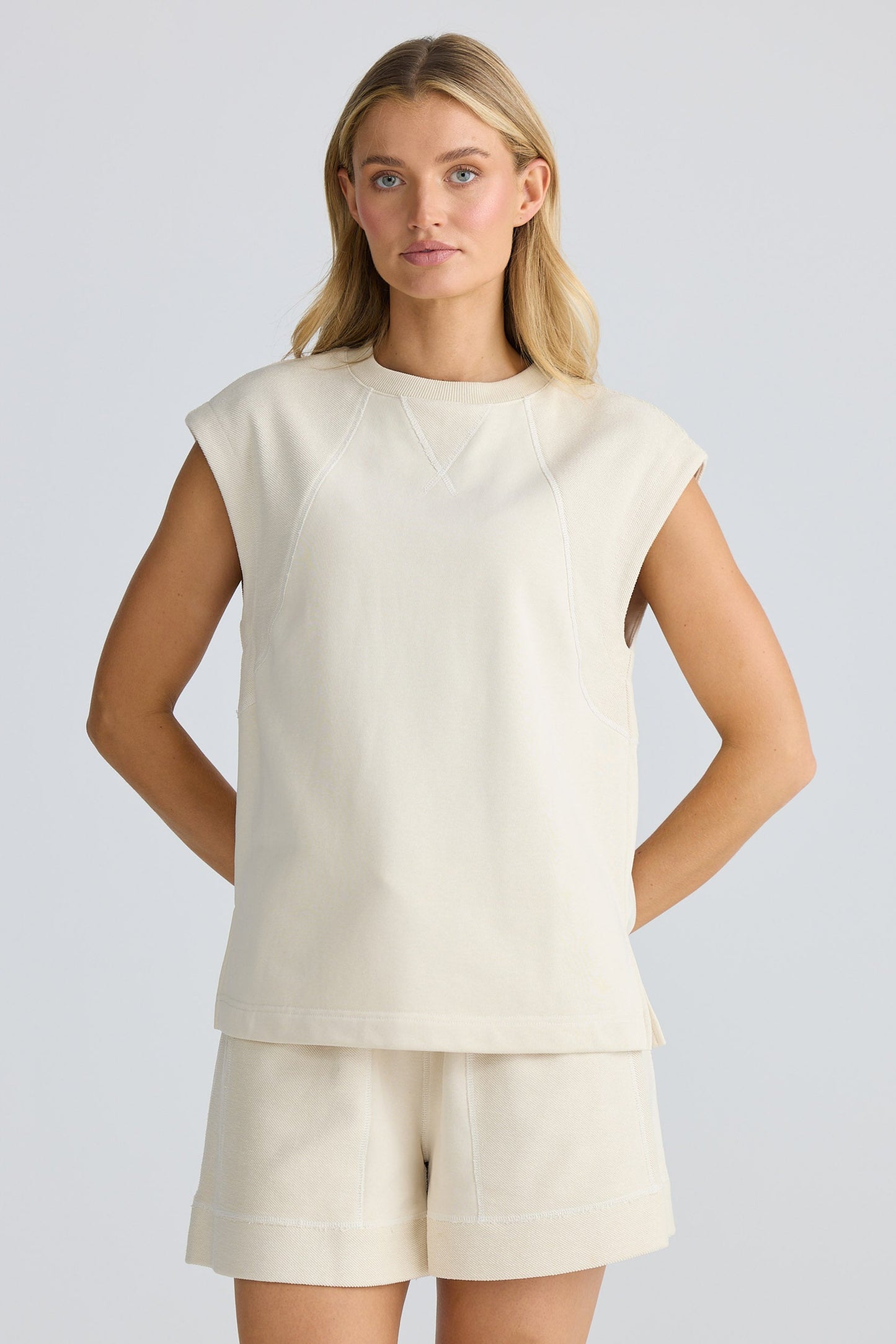 Woman wearing a cream-colored sleeveless top and shorts on a light gray background