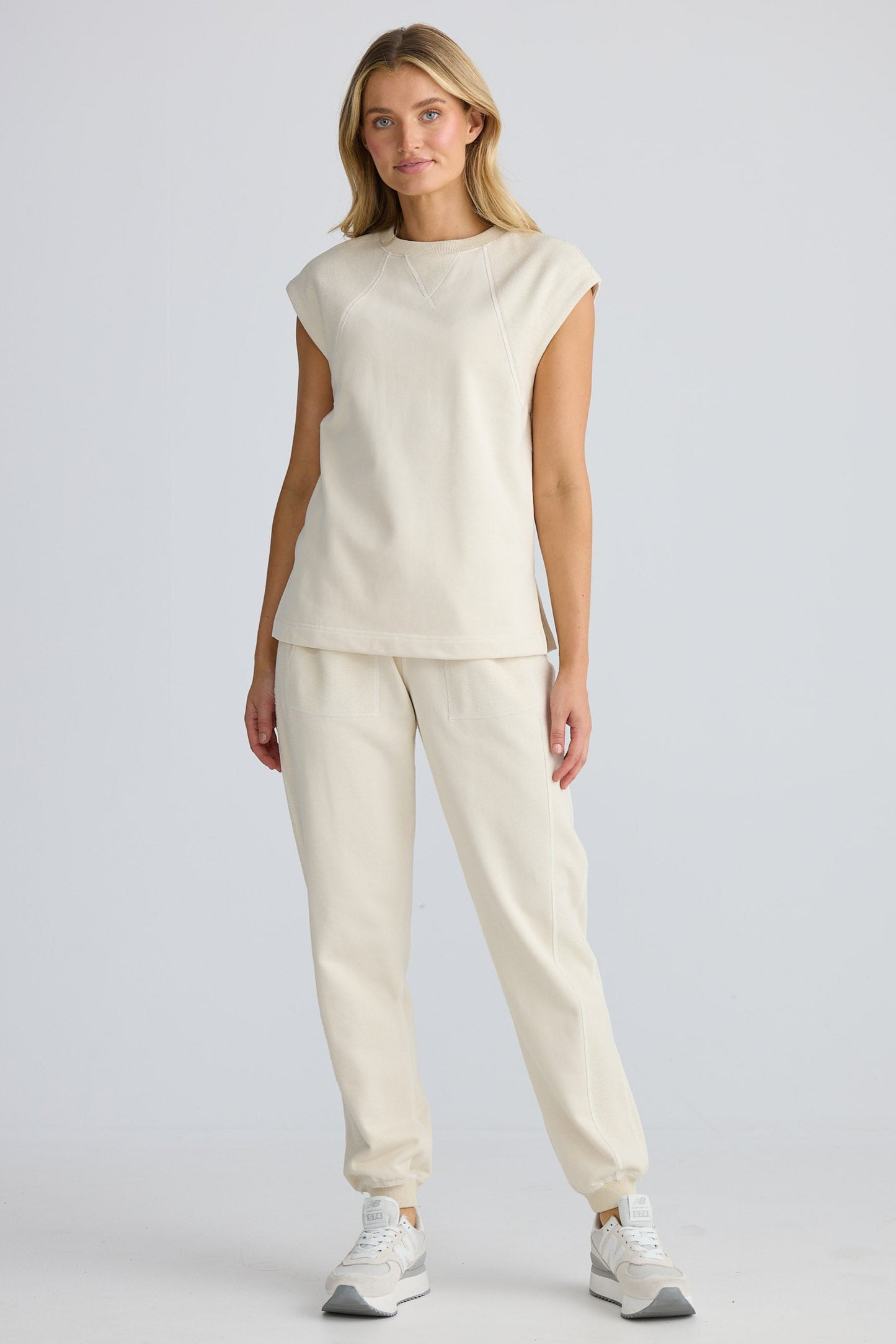 Woman wearing a beige sleeveless top and pants on a white background