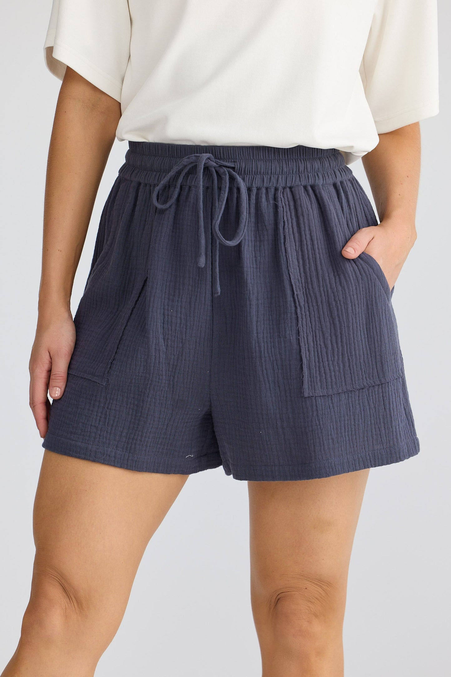 Person wearing navy shorts with a white top on a light gray background