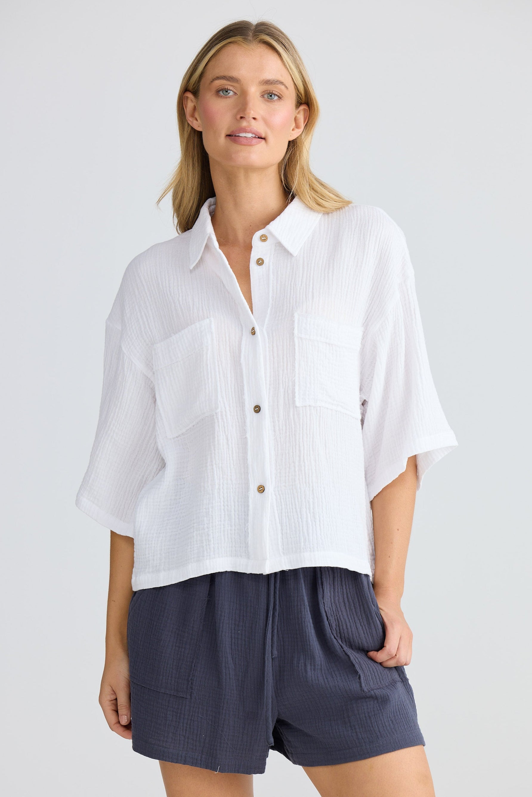 Woman wearing a white shirt and navy shorts on a plain background