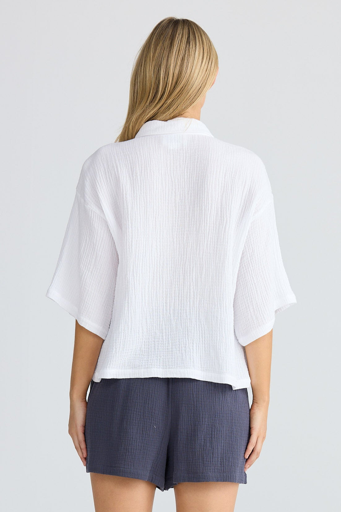 Person wearing a white shirt and navy shorts on a plain background