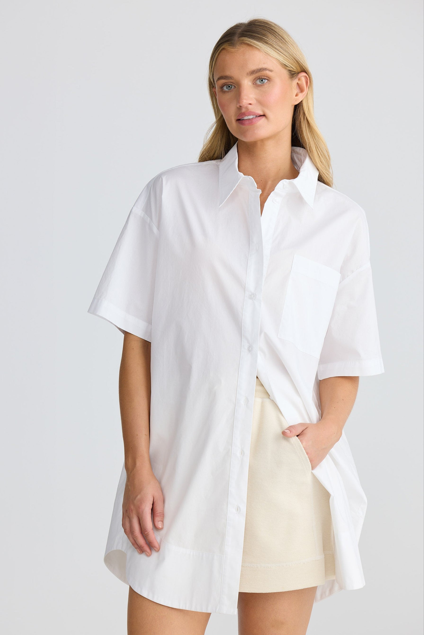 Woman wearing a white oversized shirt and beige shorts on a plain background