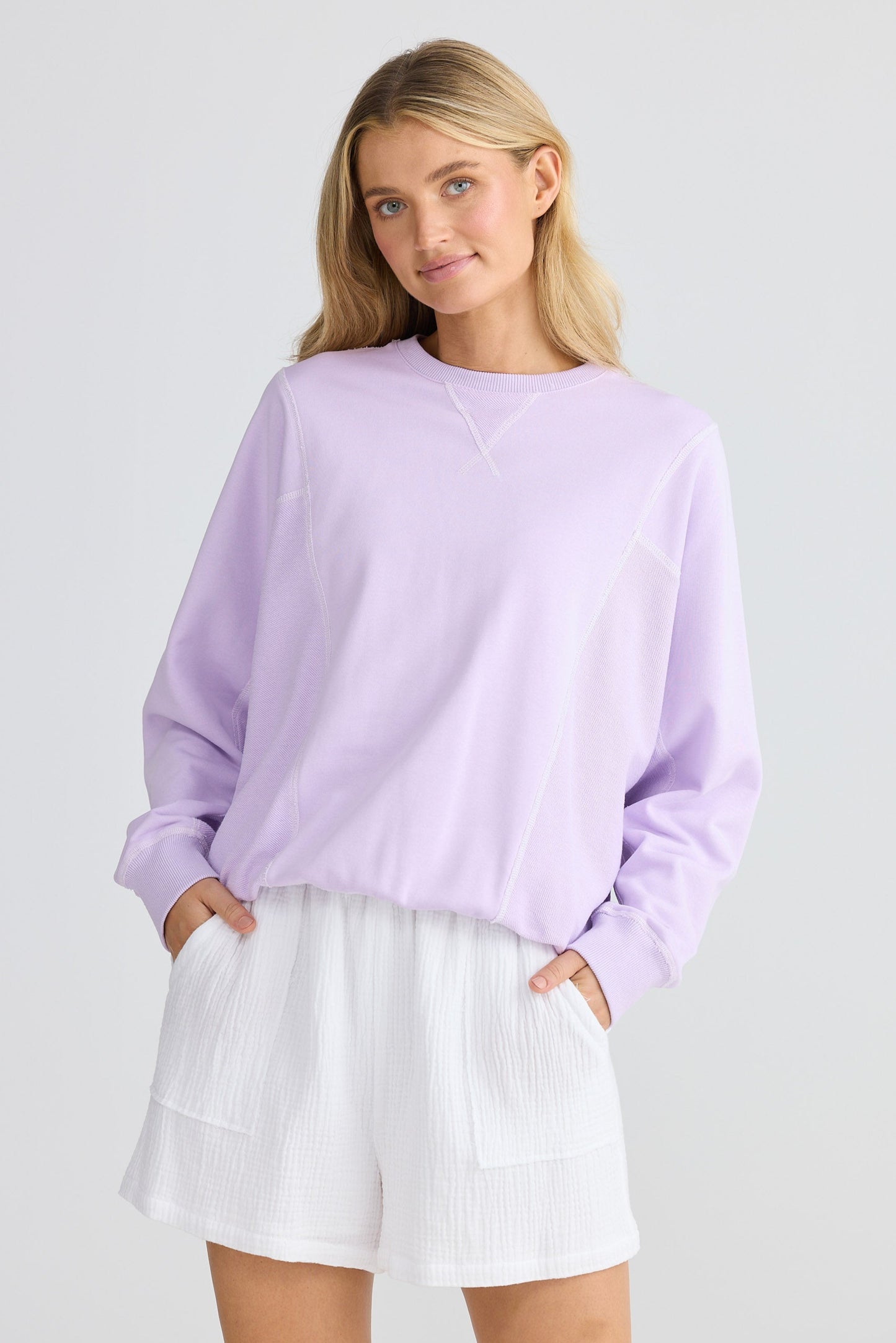 Woman wearing a light purple sweater and white skirt on a plain background