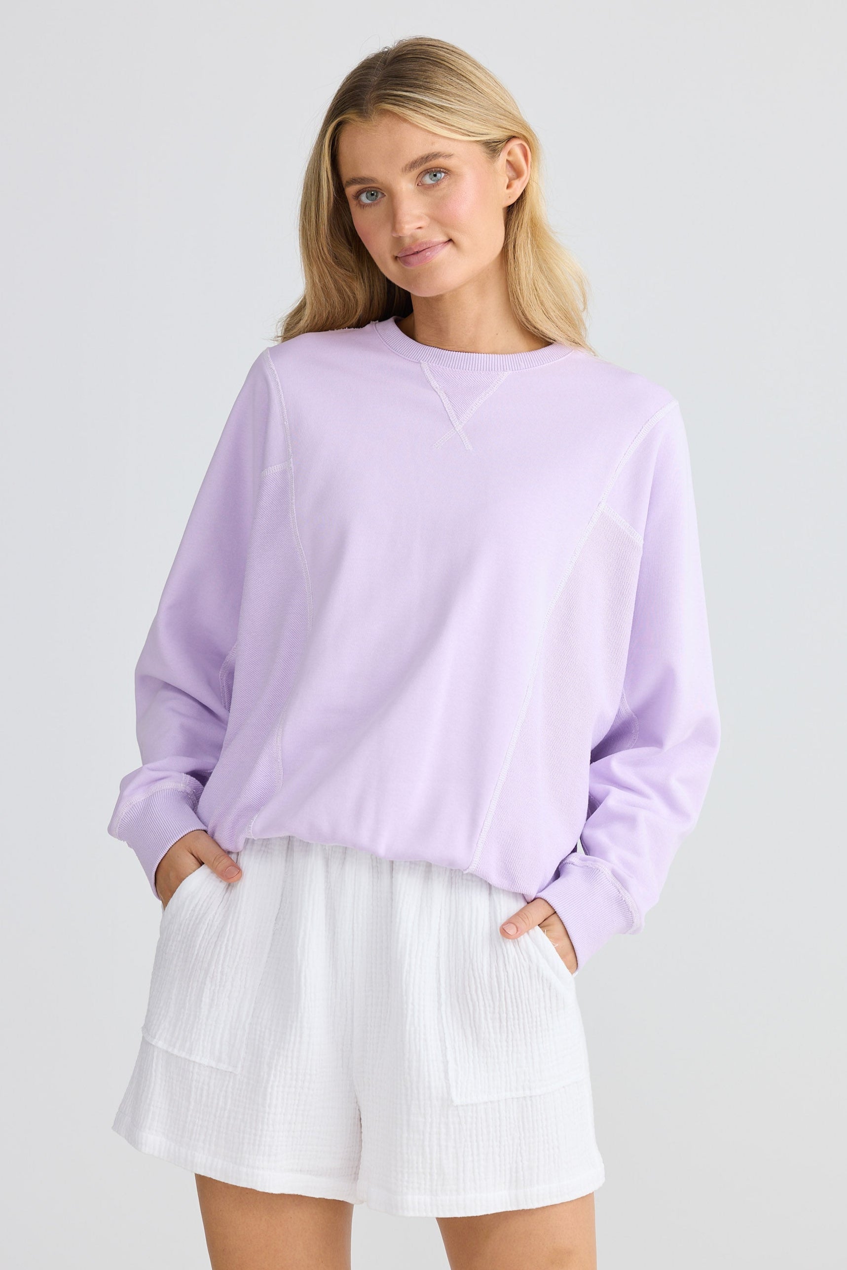 Woman wearing a light purple sweater and white skirt on a plain background