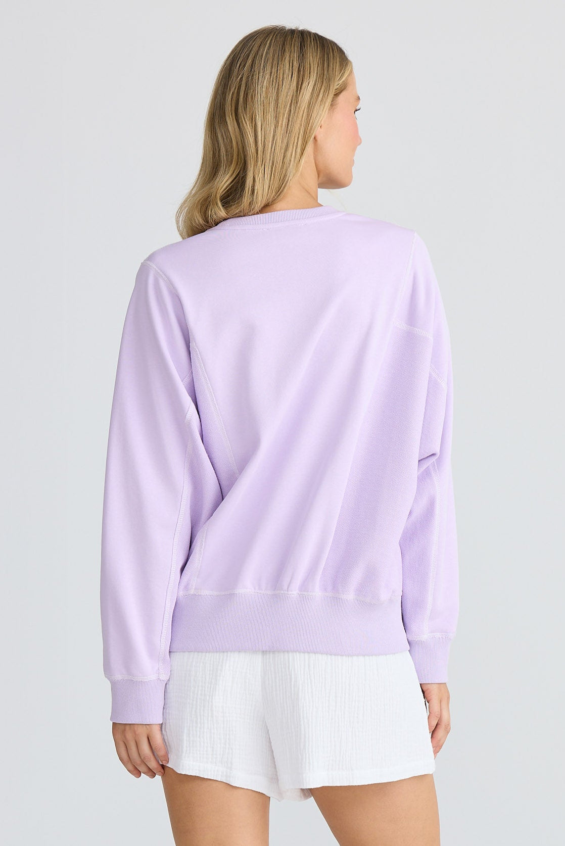 Person wearing a light purple sweatshirt and white shorts on a plain background