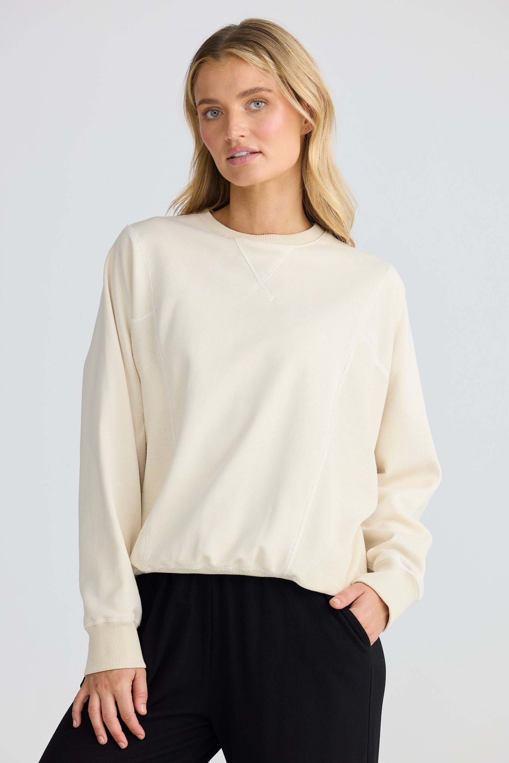 Woman wearing a cream sweater and black pants on a white background